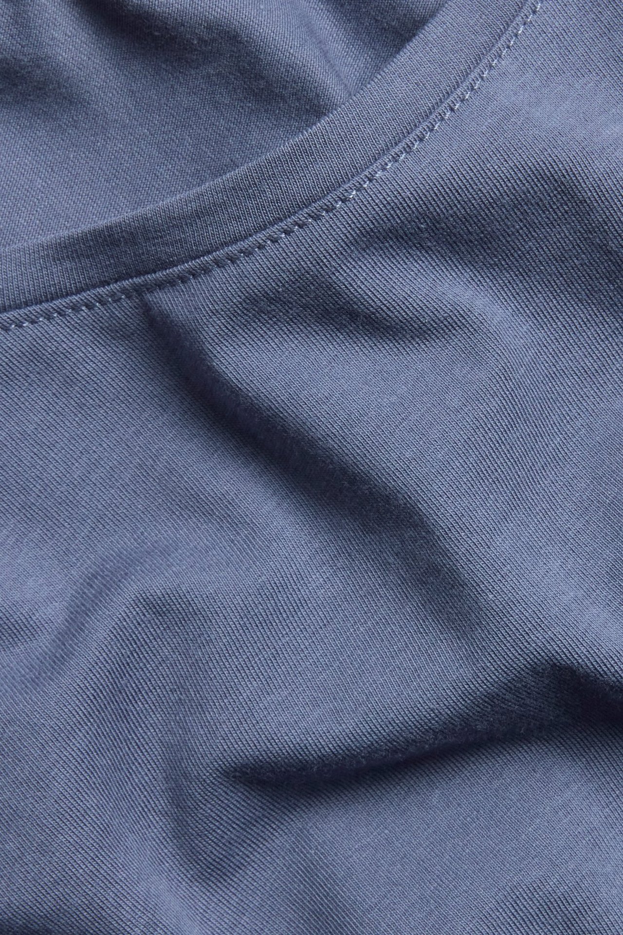 Zbliżenie niebieskiego, długiego topu z okrągłym dekoltem, wykonanego z gładkiej mieszanki bawełny.