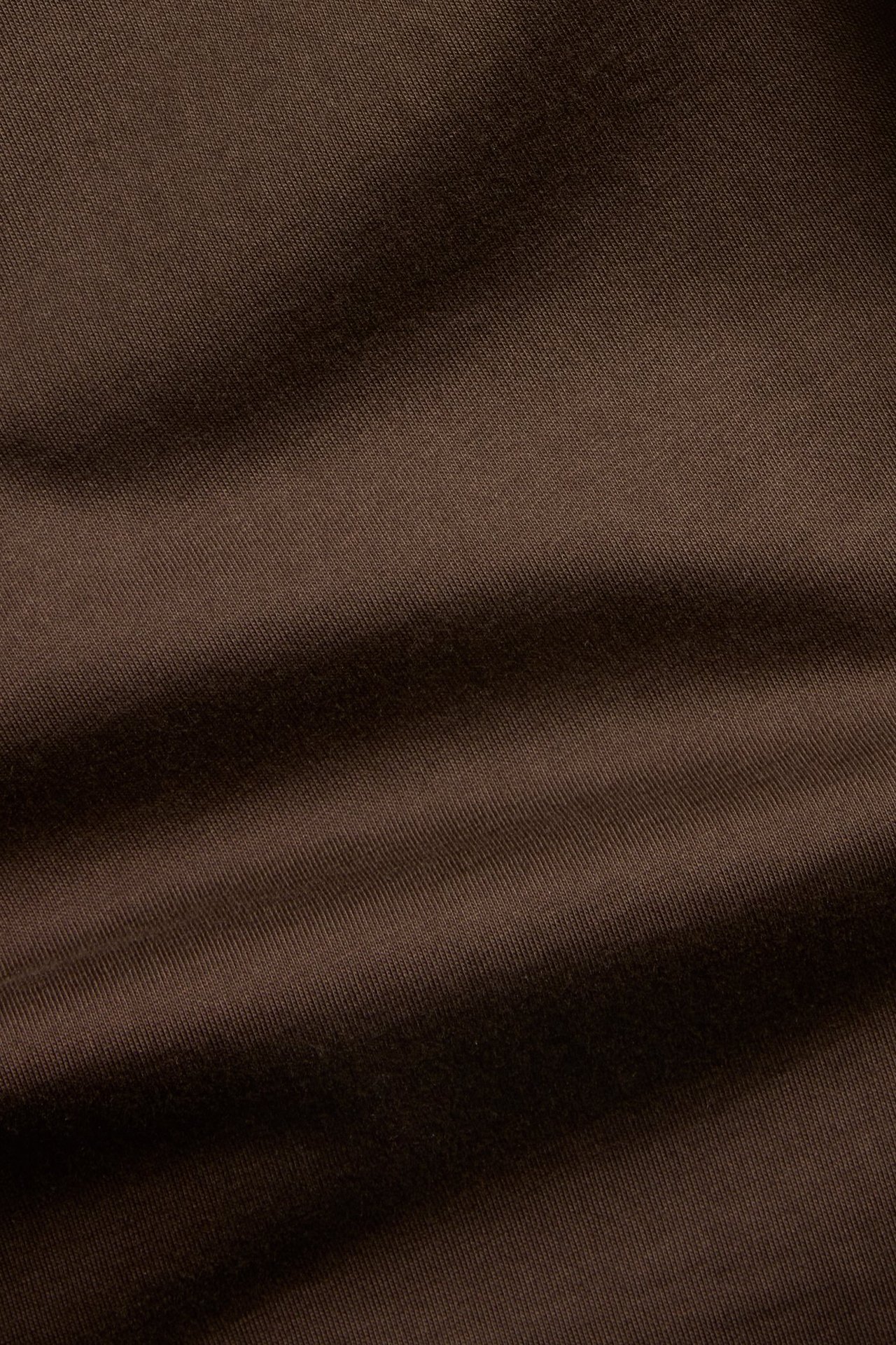 Zbliżenie ciemnobrązowego, jednolitego materiału bawełnianego o prostym kroju, odpowiedniego na T-shirt.