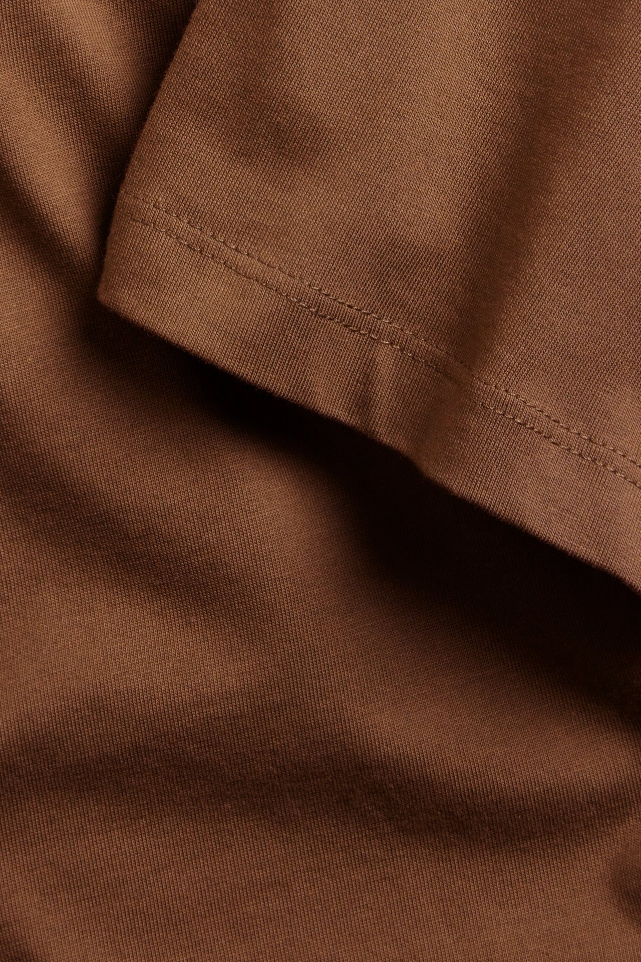 Zbliżenie na brązowy, jednolity bawełniany T-shirt z widocznymi szwami.
