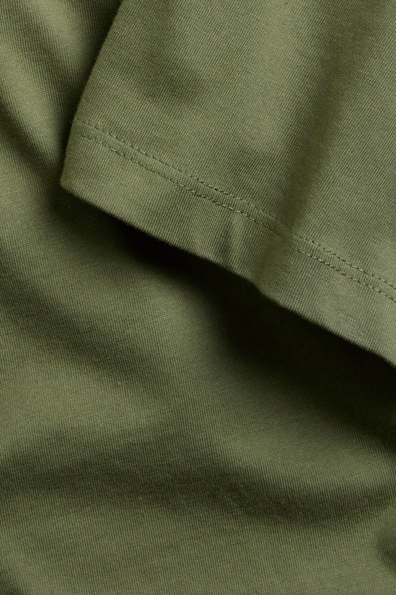 Zbliżenie zielonej bawełnianej tkaniny T-shirtu z widocznym szwem.