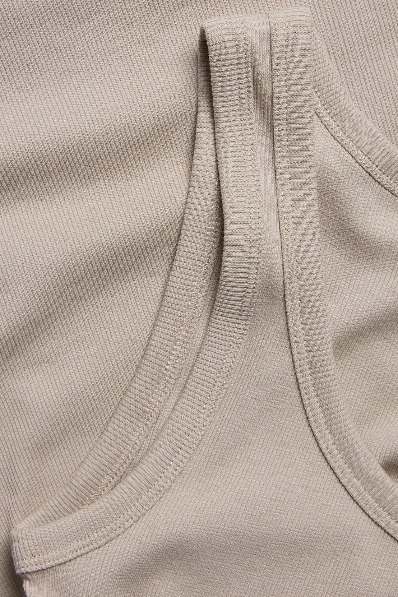 Zbliżenie beżowego prążkowanego topu, ukazujące teksturowaną tkaninę z mieszanki bawełny i dekolt.