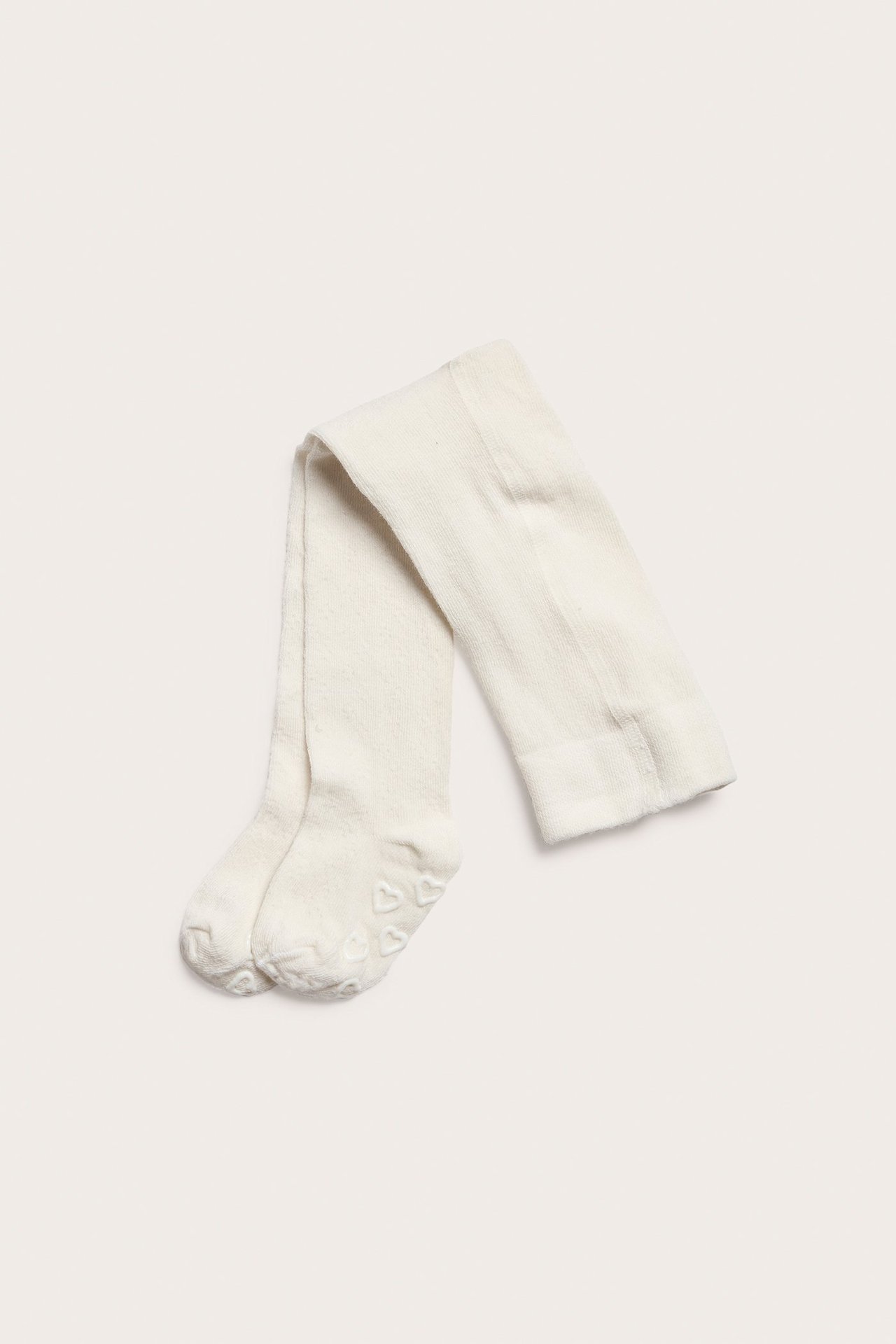 Ovanifrån, vikta offwhite baby strumpbyxor med halkskyddande hjärtmönster på sulorna.