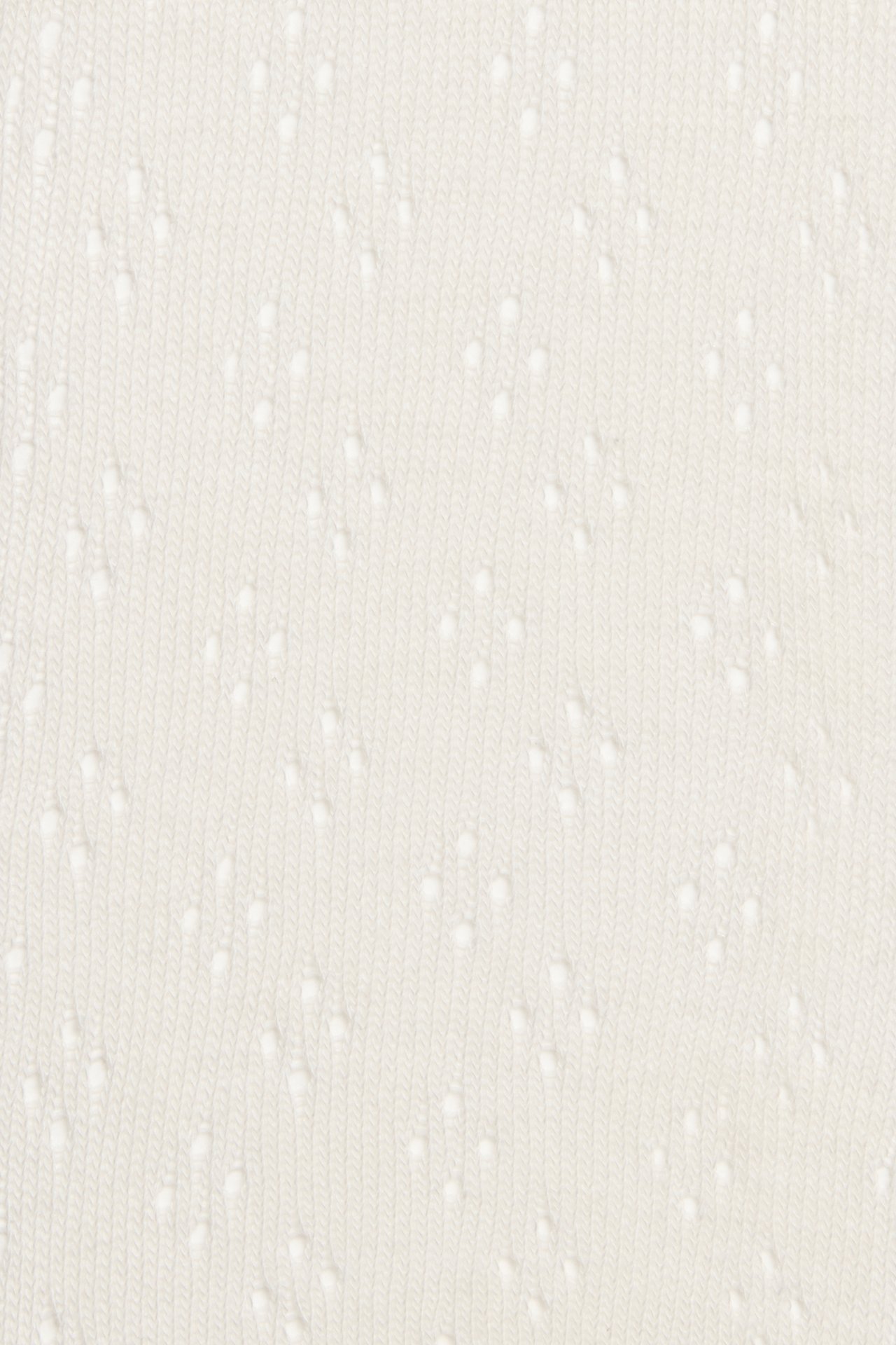 Nærbilde av offwhite strikket strømpebuksemateriale med diskret hullmønster.