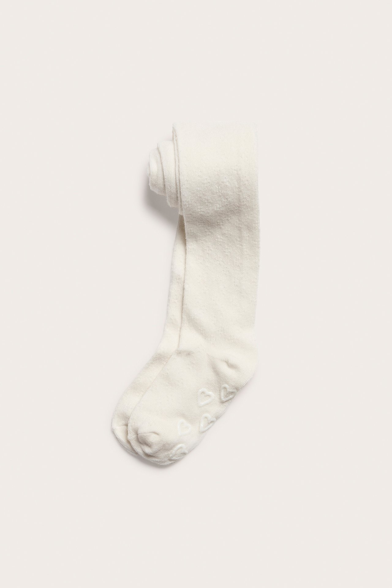 Ovenfra: Offwhite babystrømpebukser med diskret hullmønster og antiskli-hjerter på sålene.