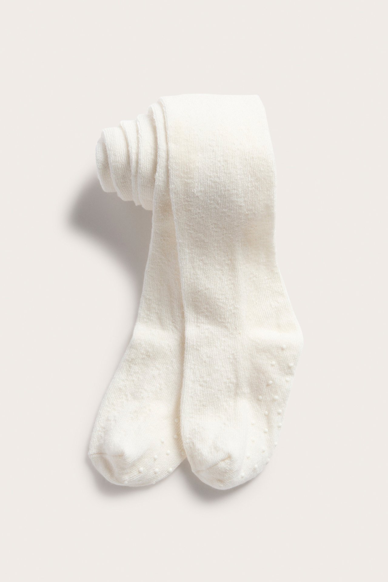 Framifrån: krämvita babytights med antihalksulor, prydligt vikta.