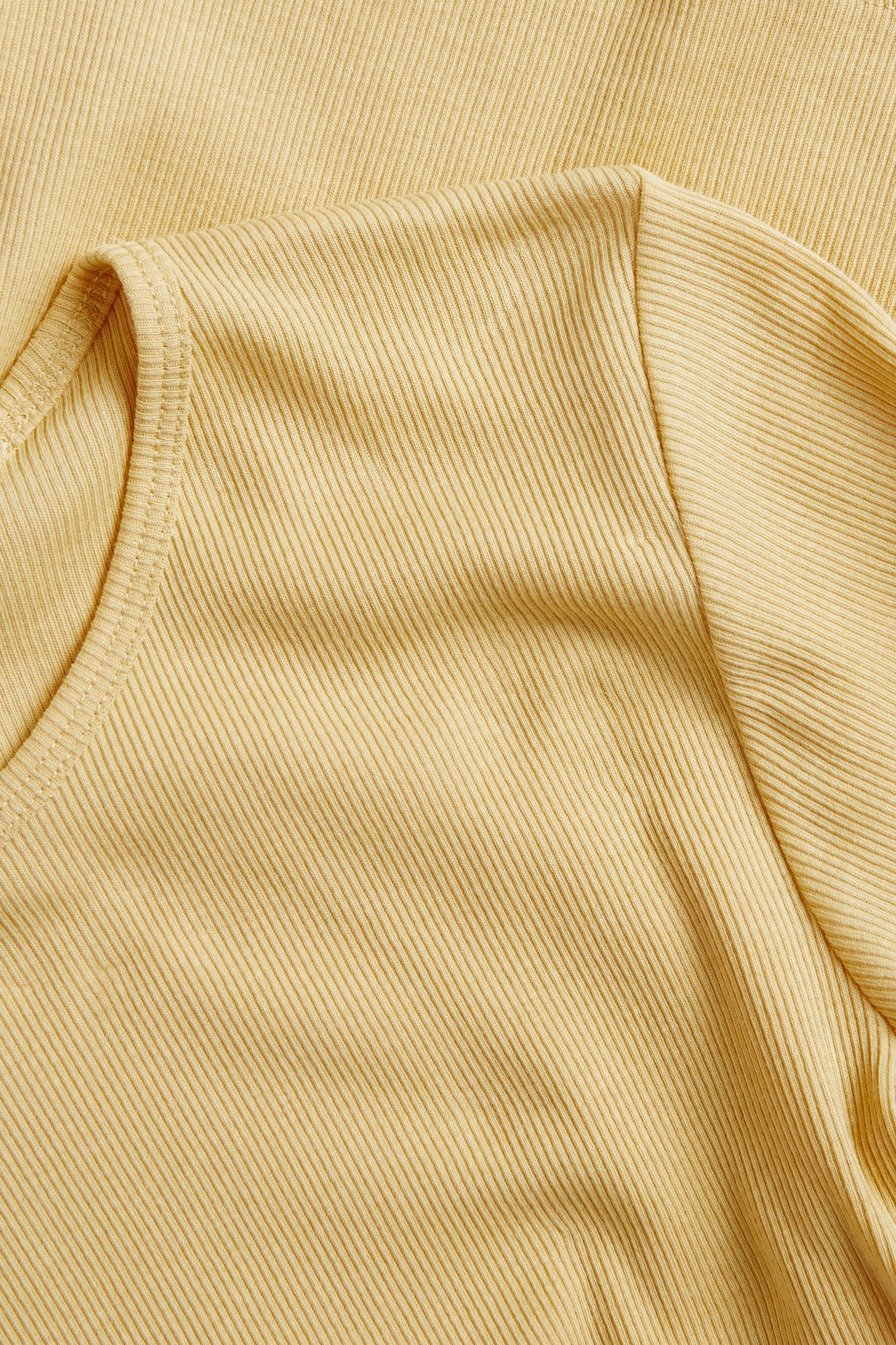 Zbliżenie na jasnożółty, prążkowany, dopasowany T-shirt z krótkim rękawem.