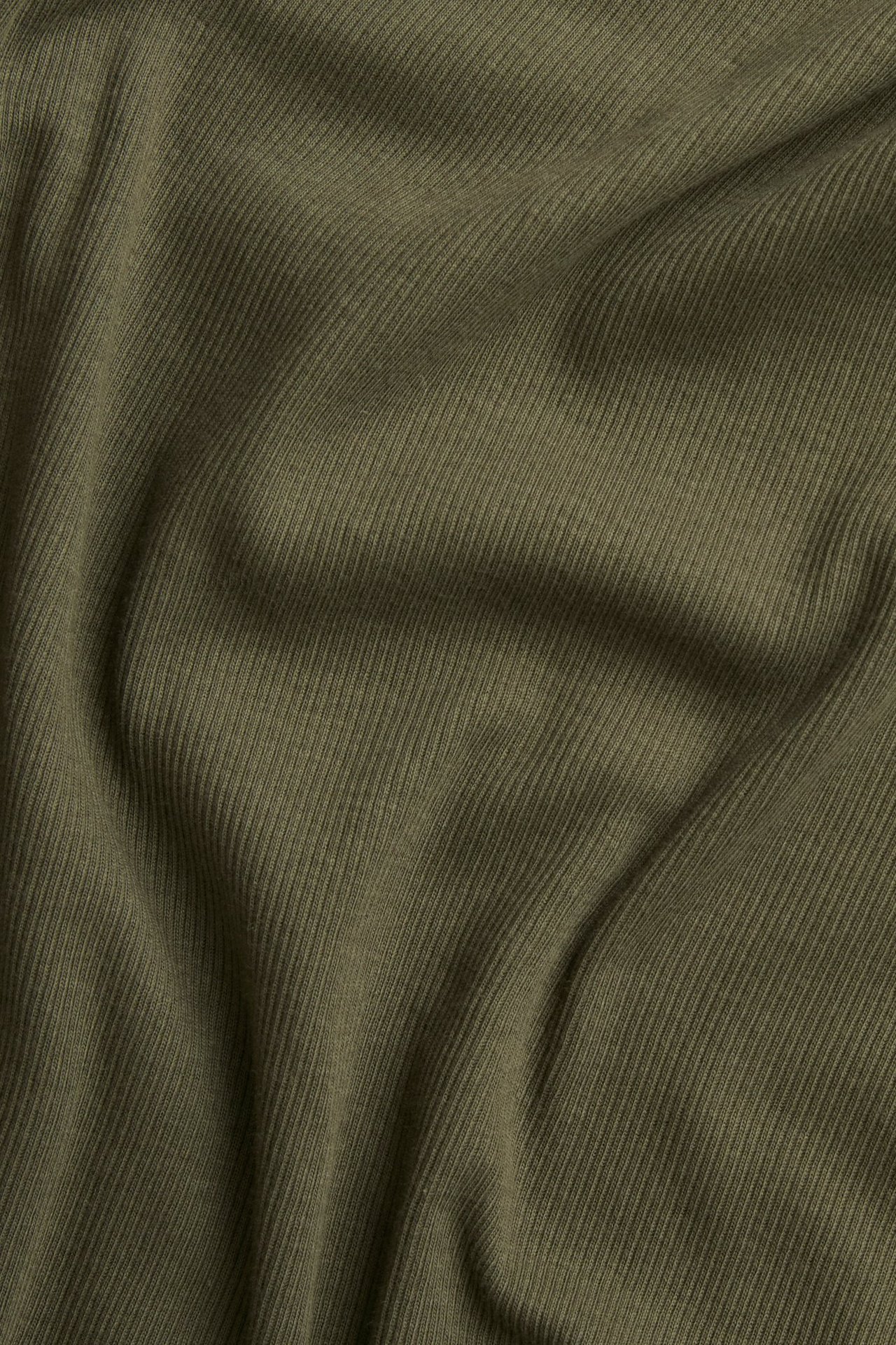 Zbliżenie zielonego prążkowanego materiału bluzki z długim rękawem, ukazujące jego fakturę.