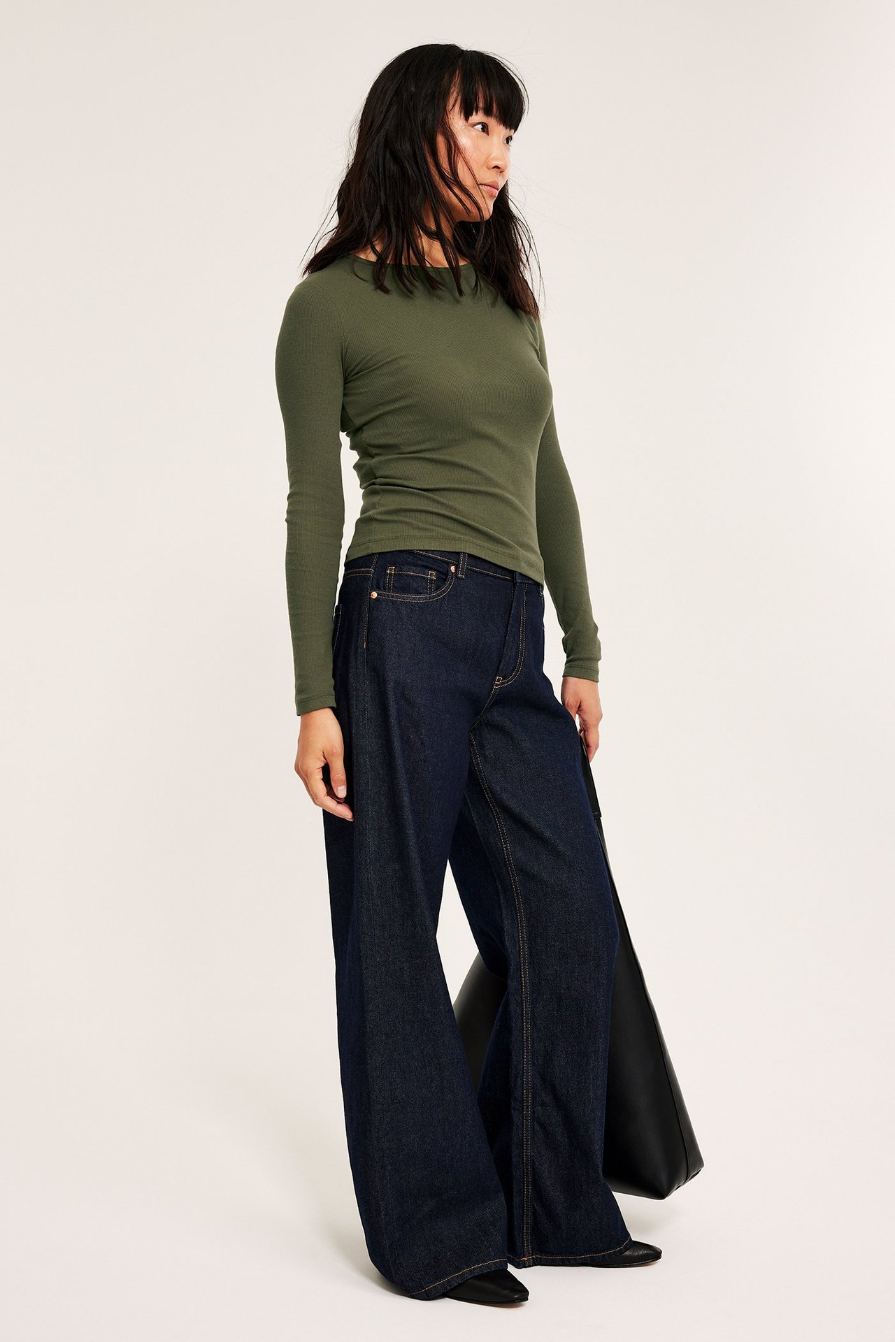 Kobieta w zielonej długie rękawy, strukturalnej koszulce z okrągłym dekoltem, ciemnych dżinsach.