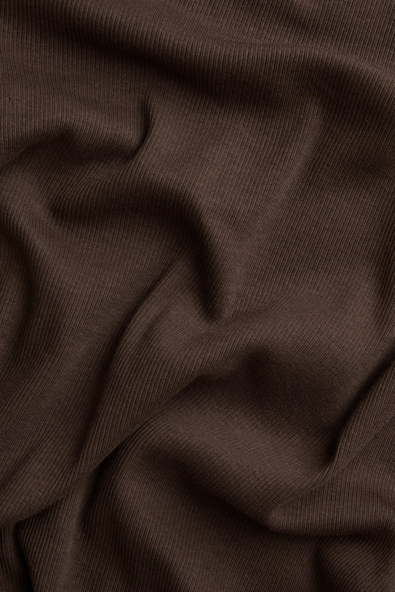 Zbliżenie na ciemnobrązowy prążkowany materiał bluzki z długim rękawem o wąskiej strukturze żeberkowej.