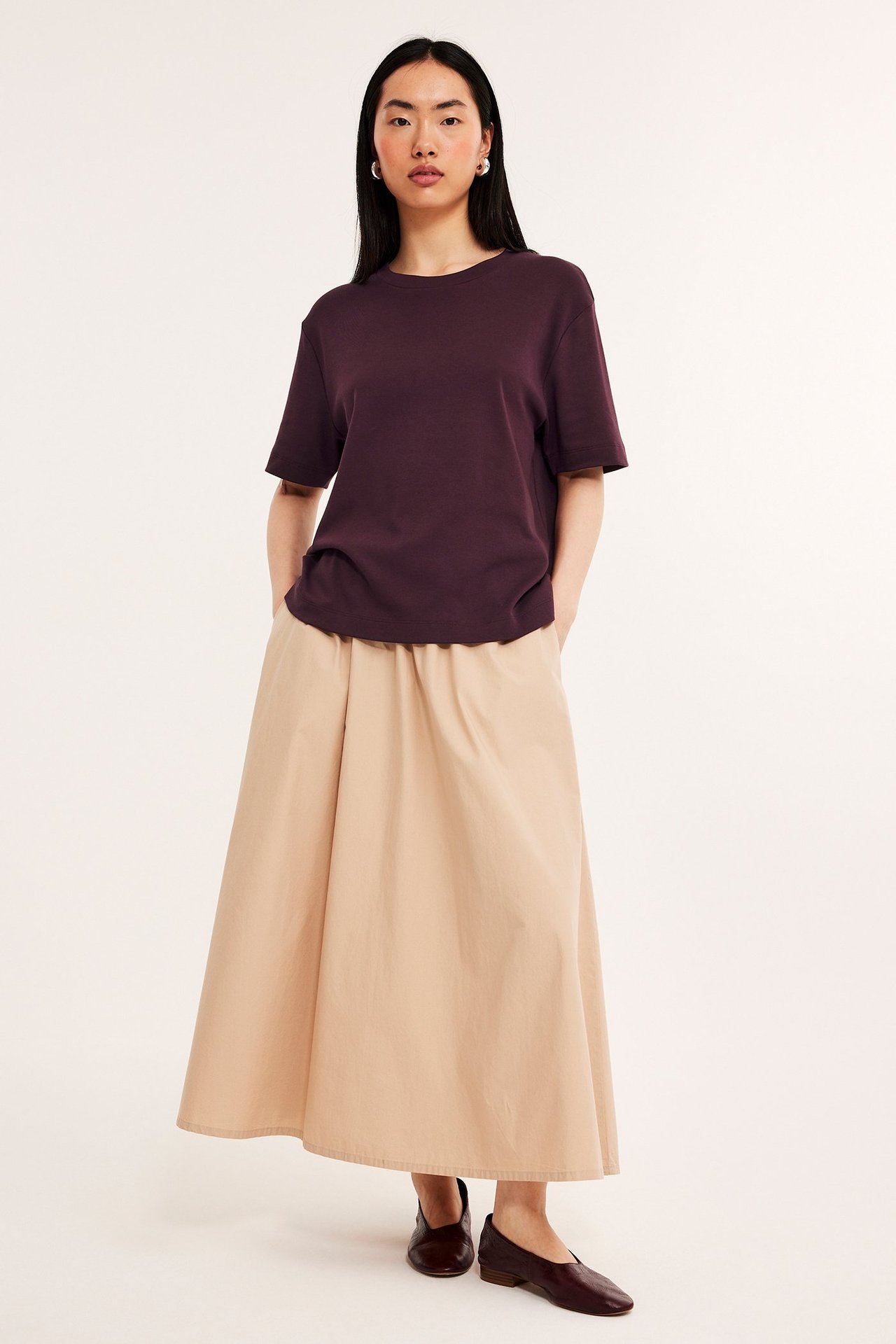 Forfra: Kvinne i mørkerød oversized T-skjorte, beige skjørt og mørkerøde flate sko.