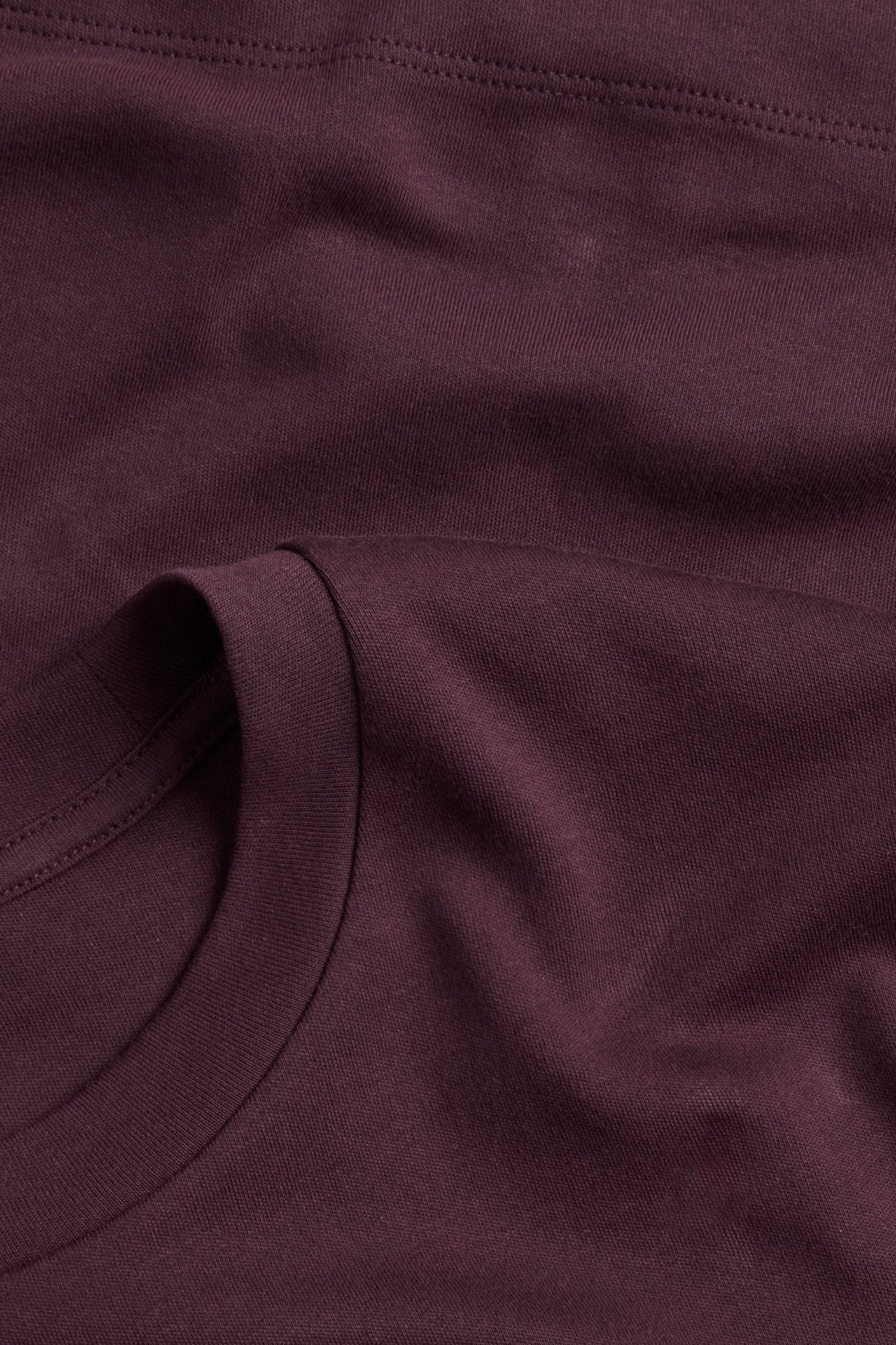 Zbliżenie na ciemnoczerwony, jednolity t-shirt z bawełnianego interlocku, ukazujące okrągły dekolt i fakturę materiału.