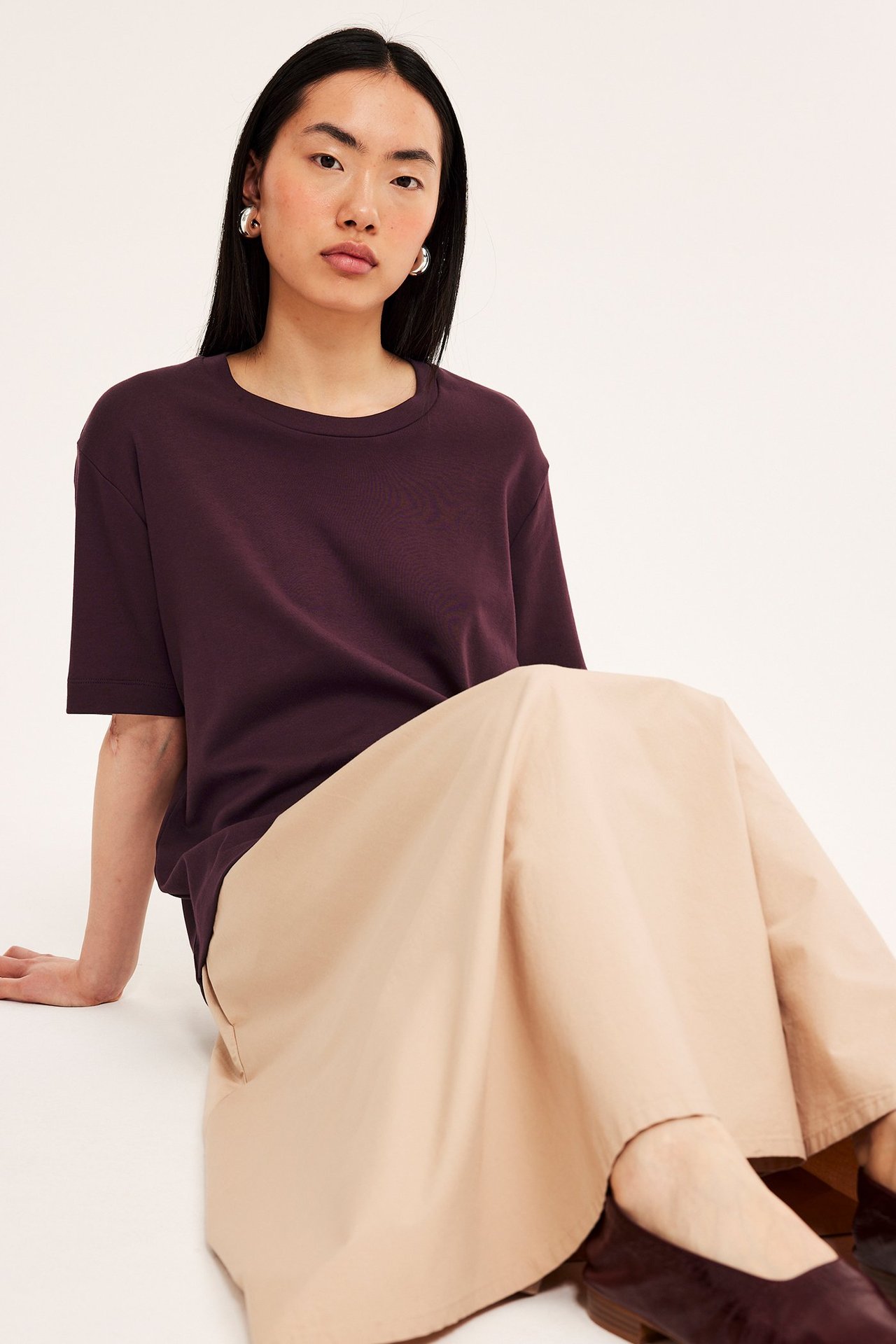 Forfra: Kvinne i mørkerød oversized bomulls-t-skjorte, beige vide bukser og mørkerøde flate sko.