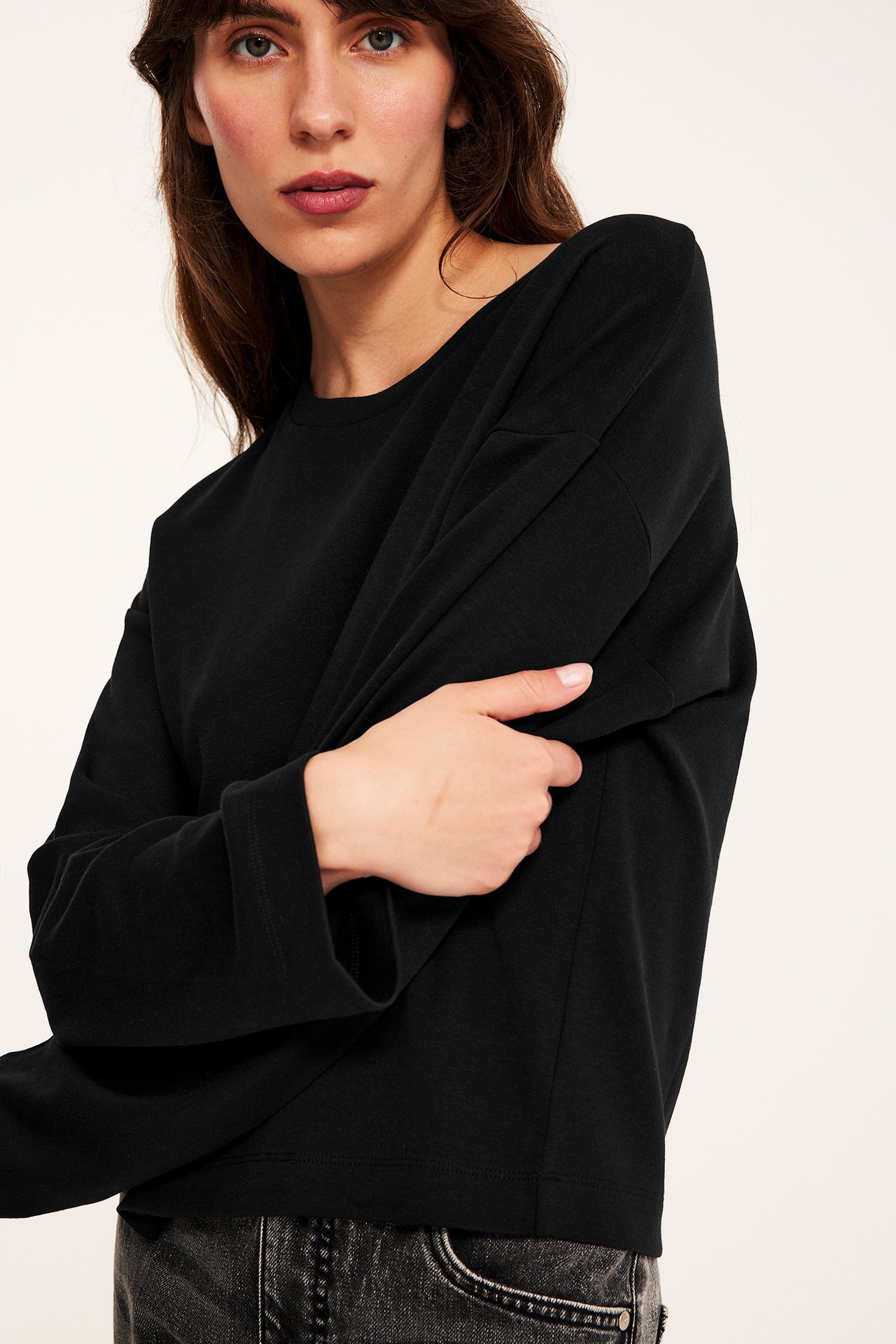Nærbilde forfra av en kvinne i en svart løs langermet t-skjorte i bomull og mørke jeans.