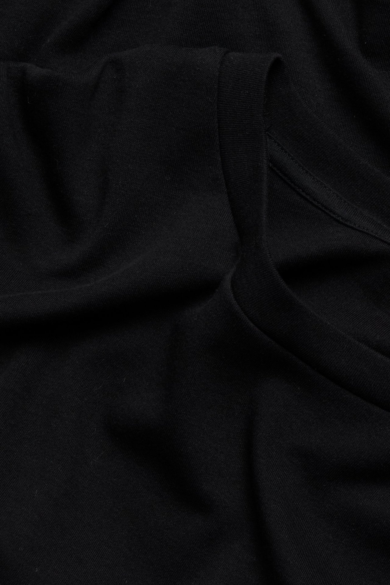 Zbliżenie na czarny, jednolity, bawełniany t-shirt z długim rękawem z widocznym dekoltem.