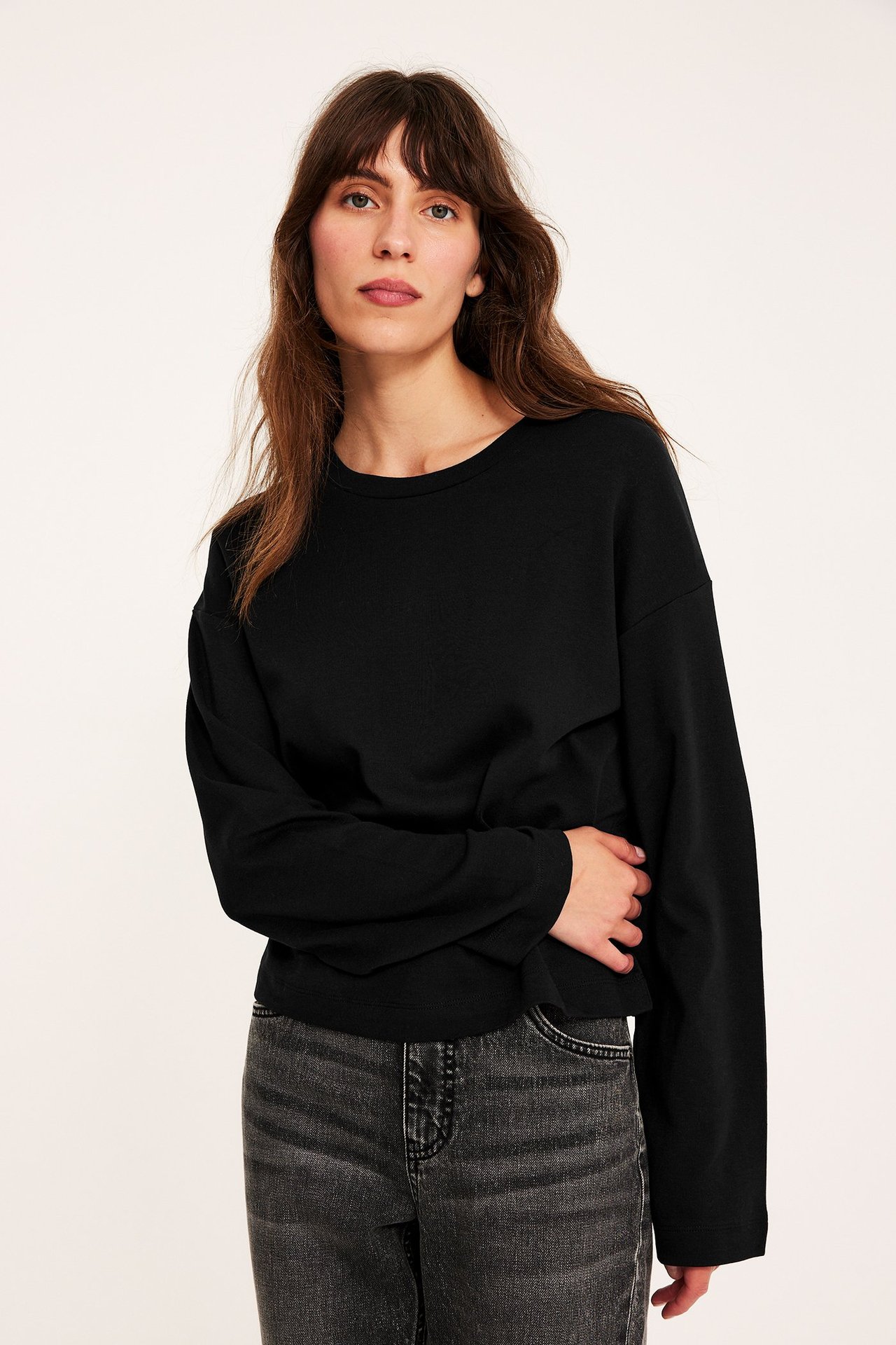 Widok z przodu: kobieta w luźnym czarnym bawełnianym T-shircie z długim rękawem i szarych jeansach.