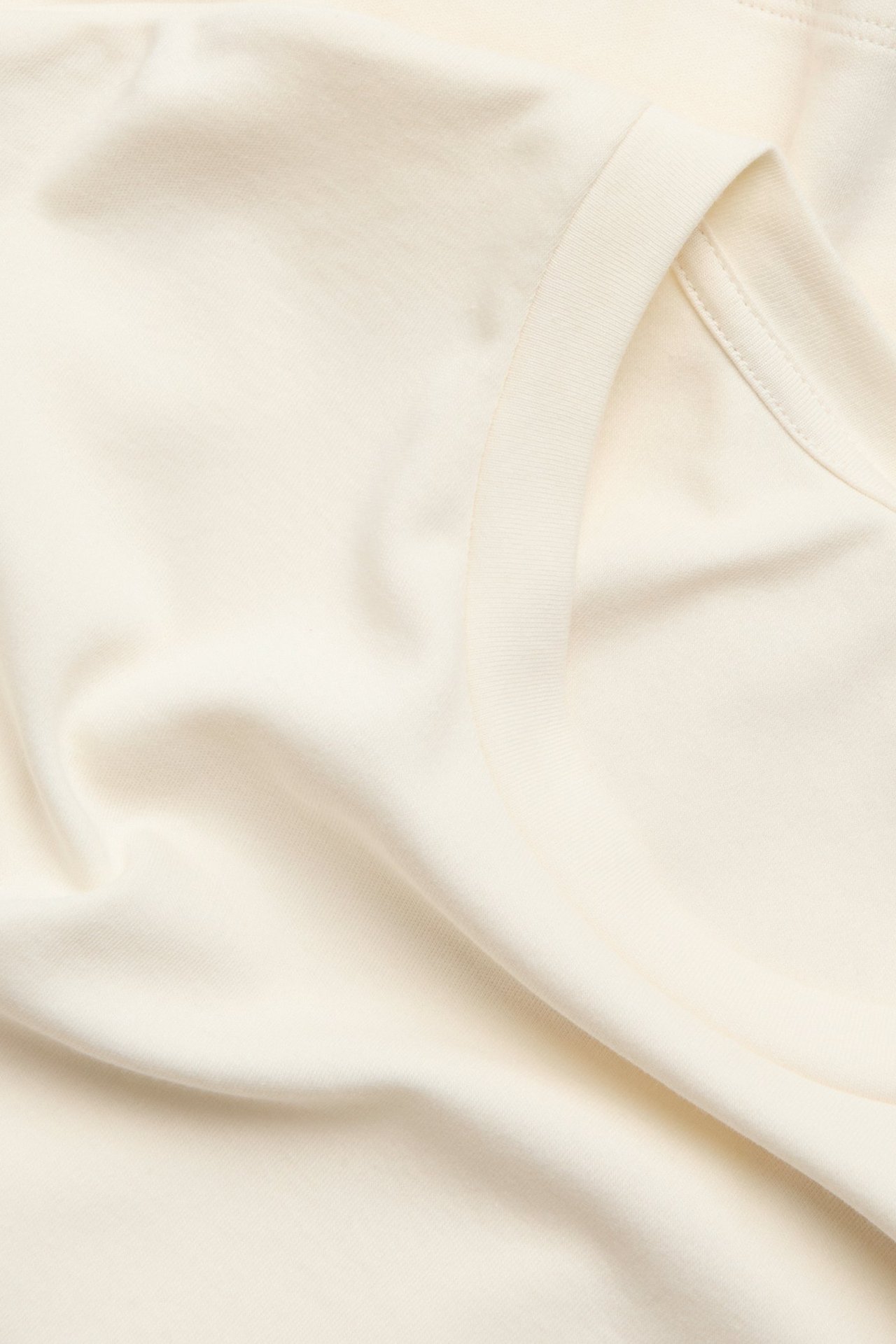Zbliżenie na luźny, długi rękaw, bawełniany T-shirt w kolorze ecru z widocznym szwem dekoltu.