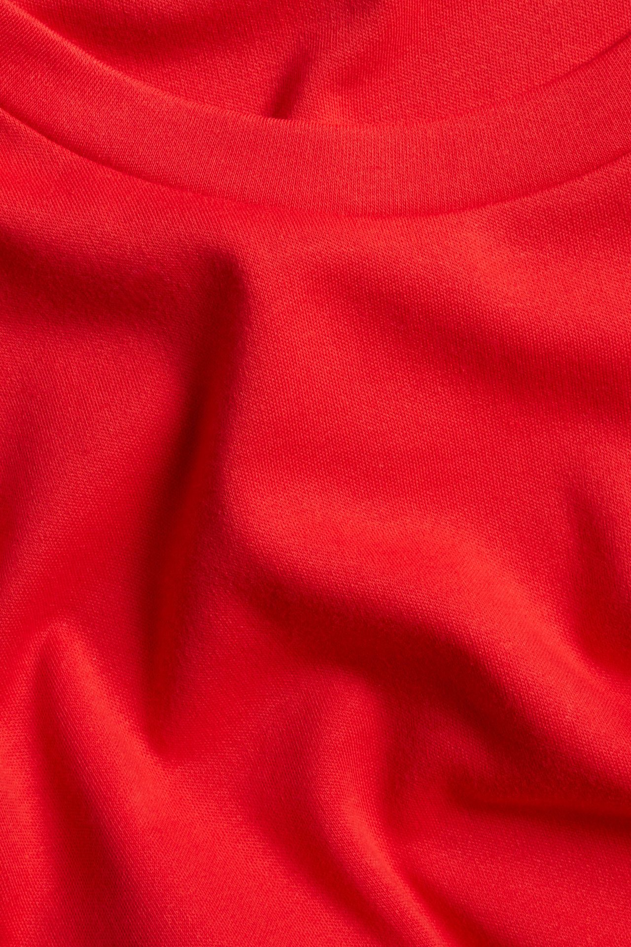 Zbliżenie na czerwoną, jednolitą, luźną koszulkę z długim rękawem z bawełnianego interlocku z dekoltem.
