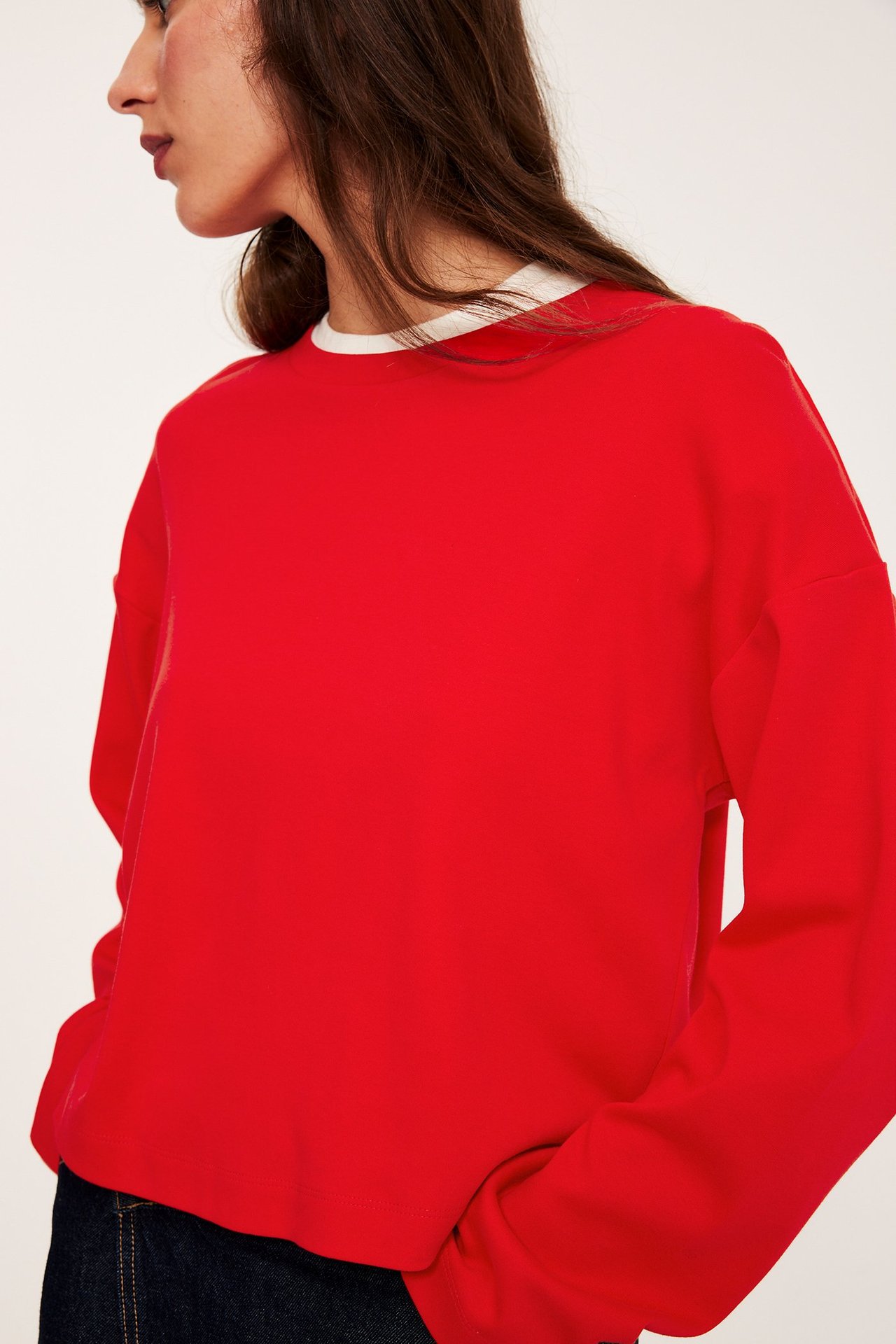 Kobieta w luźnym czerwonym t-shircie z długim rękawem, białym topie i ciemnych dżinsach.