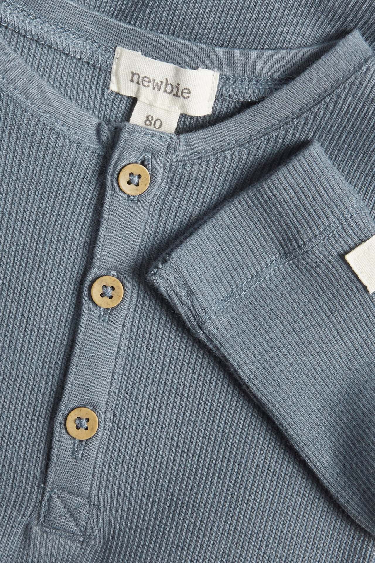 Zbliżenie niebieskiego, prążkowanego bawełnianego body niemowlęcego z długimi rękawami i trzema guzikami.