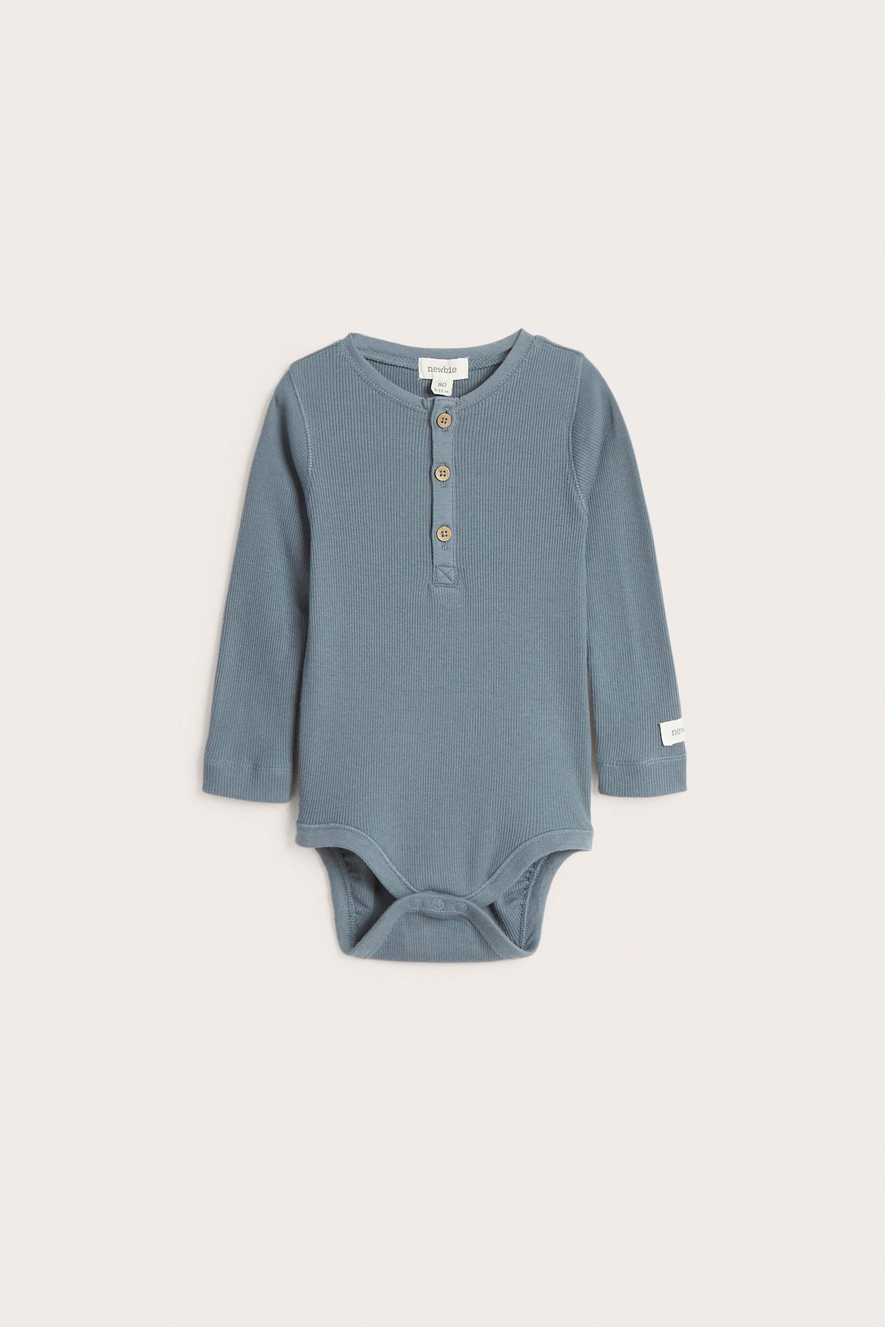 Edestä näkymä vauvan sinisestä ribatusta pitkähihaisesta body-paidasta, jossa on nappilista ja nepparit.