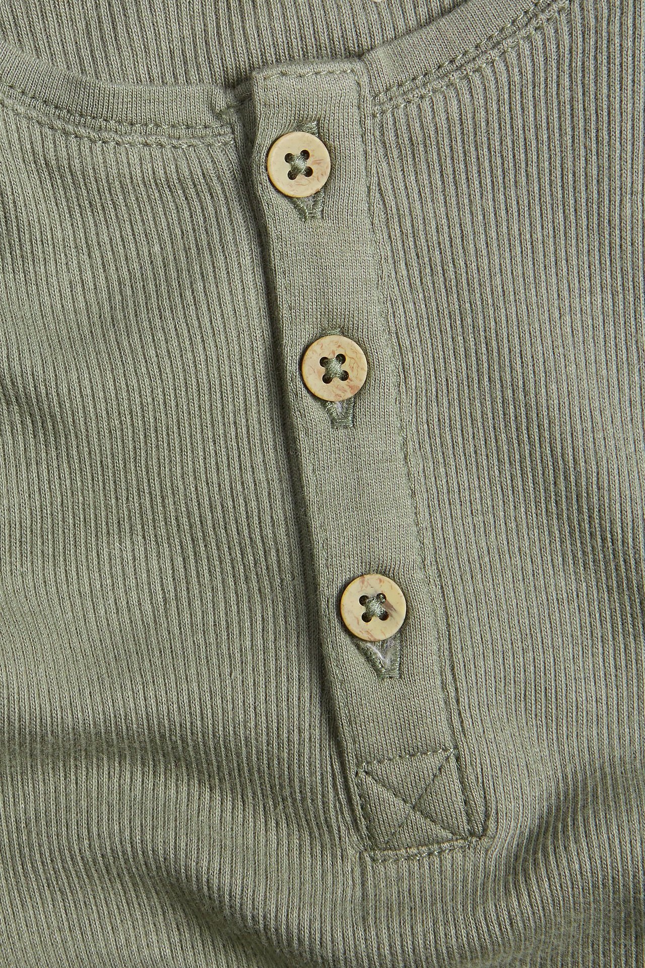 Nærbilde av en grønn ribbet bomullsbody for baby med tre knapper i knappestolpen.