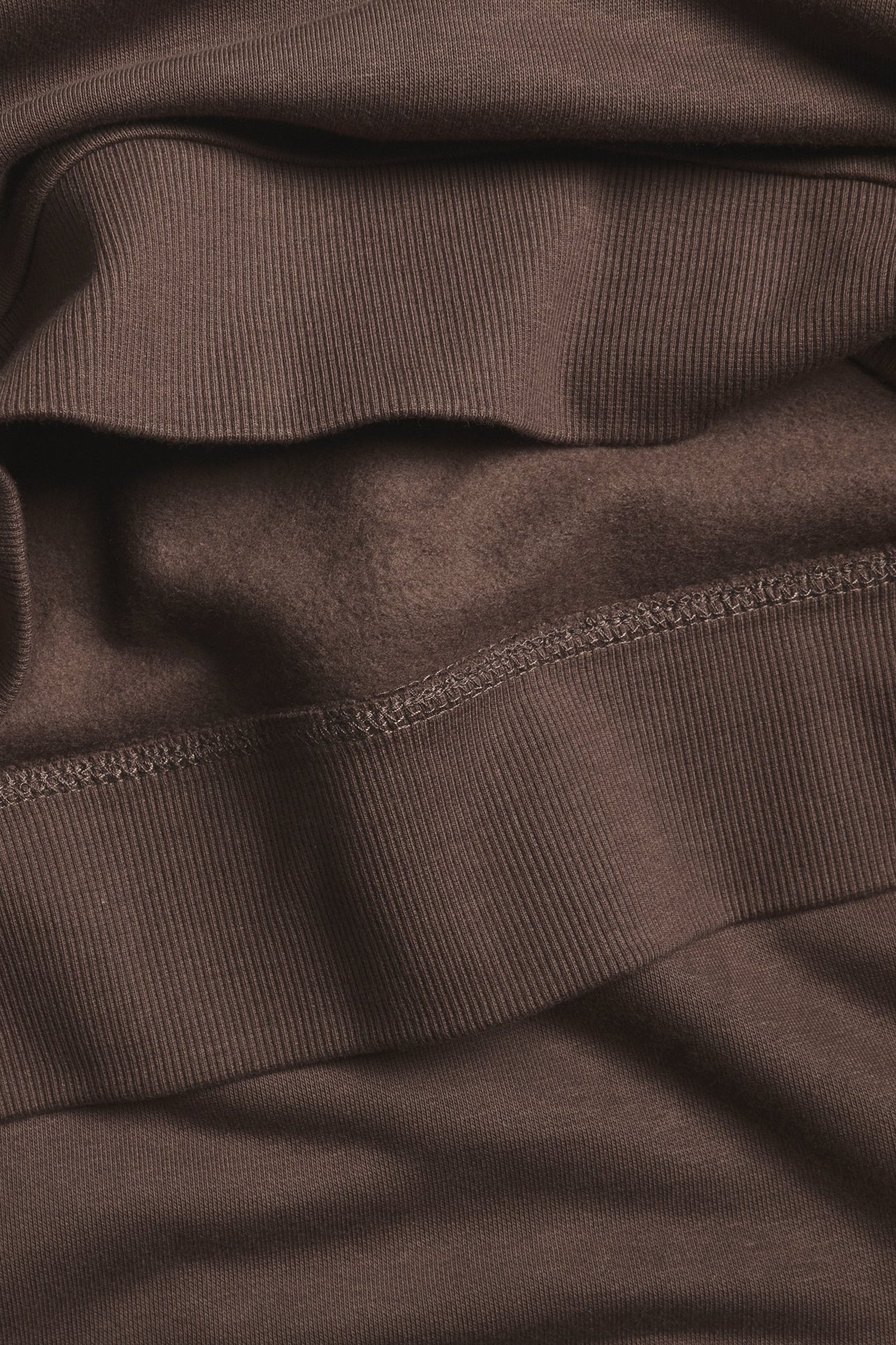 Zbliżenie na ciemnobrązową bluzę, ukazujące prążkowane mankiety i miękki, szczotkowany materiał wewnętrzny.