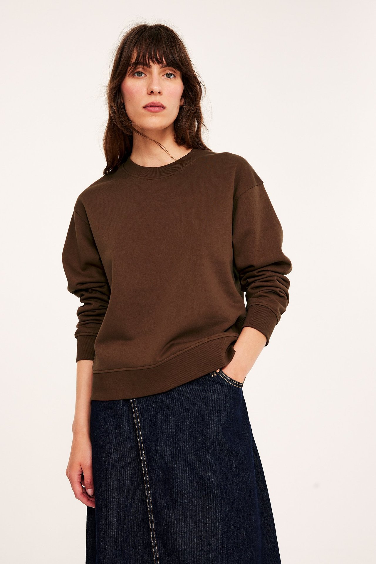 Edestä kuvattu nainen yllään ruskea pyöreäkauluksinen collegepaita ja tummansininen A-linjainen farkkuhame.