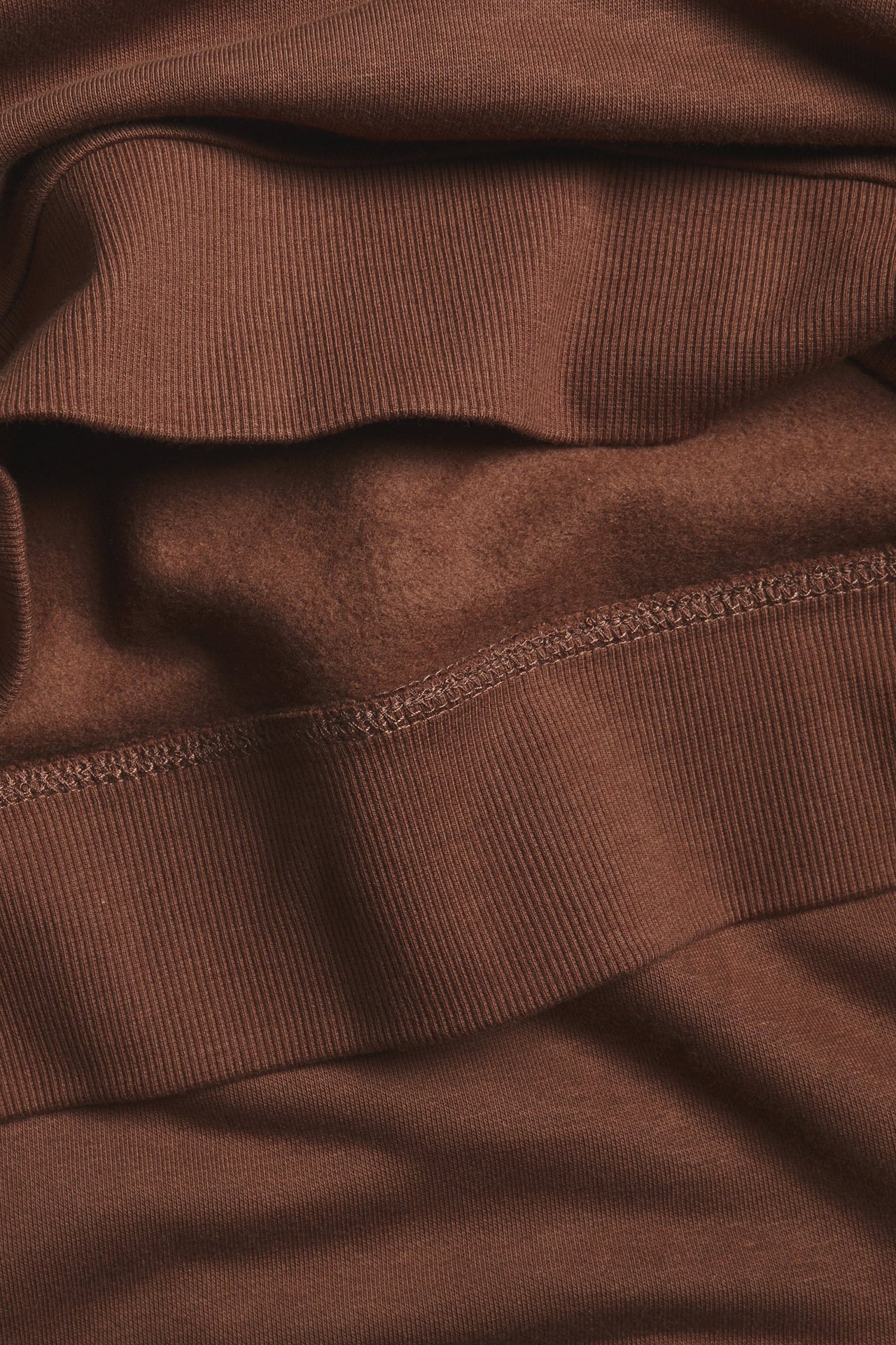 Zbliżenie brązowej bluzy, ukazujące prążkowane mankiety i miękki, szczotkowany materiał od wewnątrz.