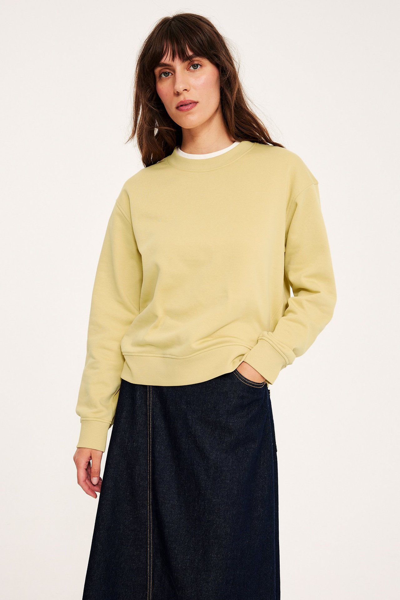 Forfra: kvinne i lys gul rundhalset sweatshirt og mørkeblått dongeriskjørt.