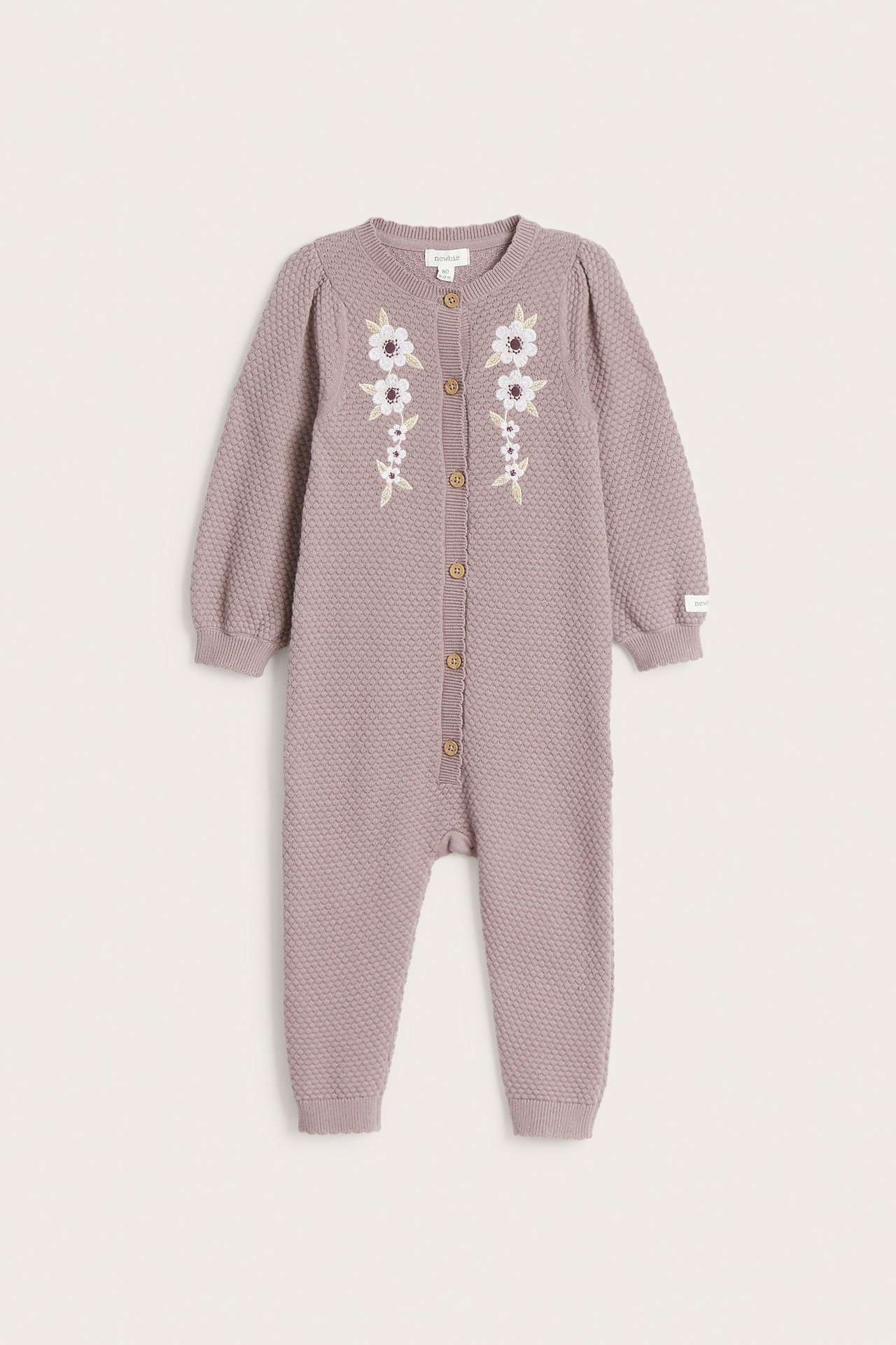 Widok z przodu jasnofioletowego bawełnianego kombinezonu niemowlęcego z haftem kwiatowym i guzikami.