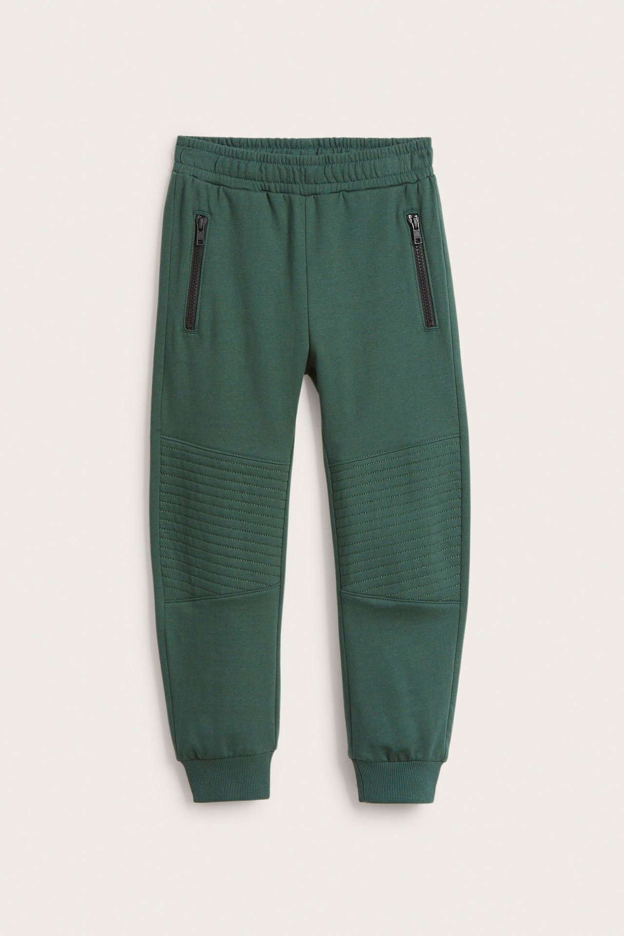 Edestä: Vihreät lasten collegehousut ribbivyötäröllä, resoreilla, mustilla vetoketjutaskuilla ja tikatuilla polvilla.