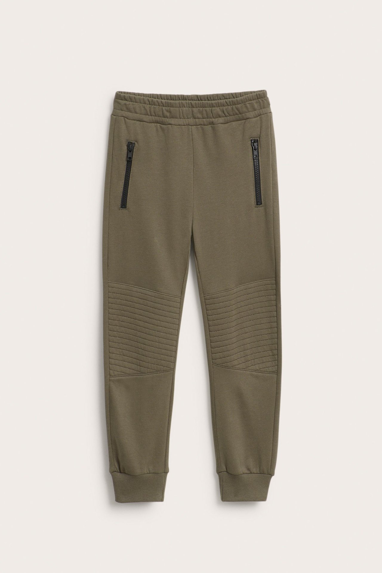 Edestä: lasten khakinväriset puuvillajoogahousut, resori vyötäröllä, tikatut polvet, mustat vetoketjutaskut.