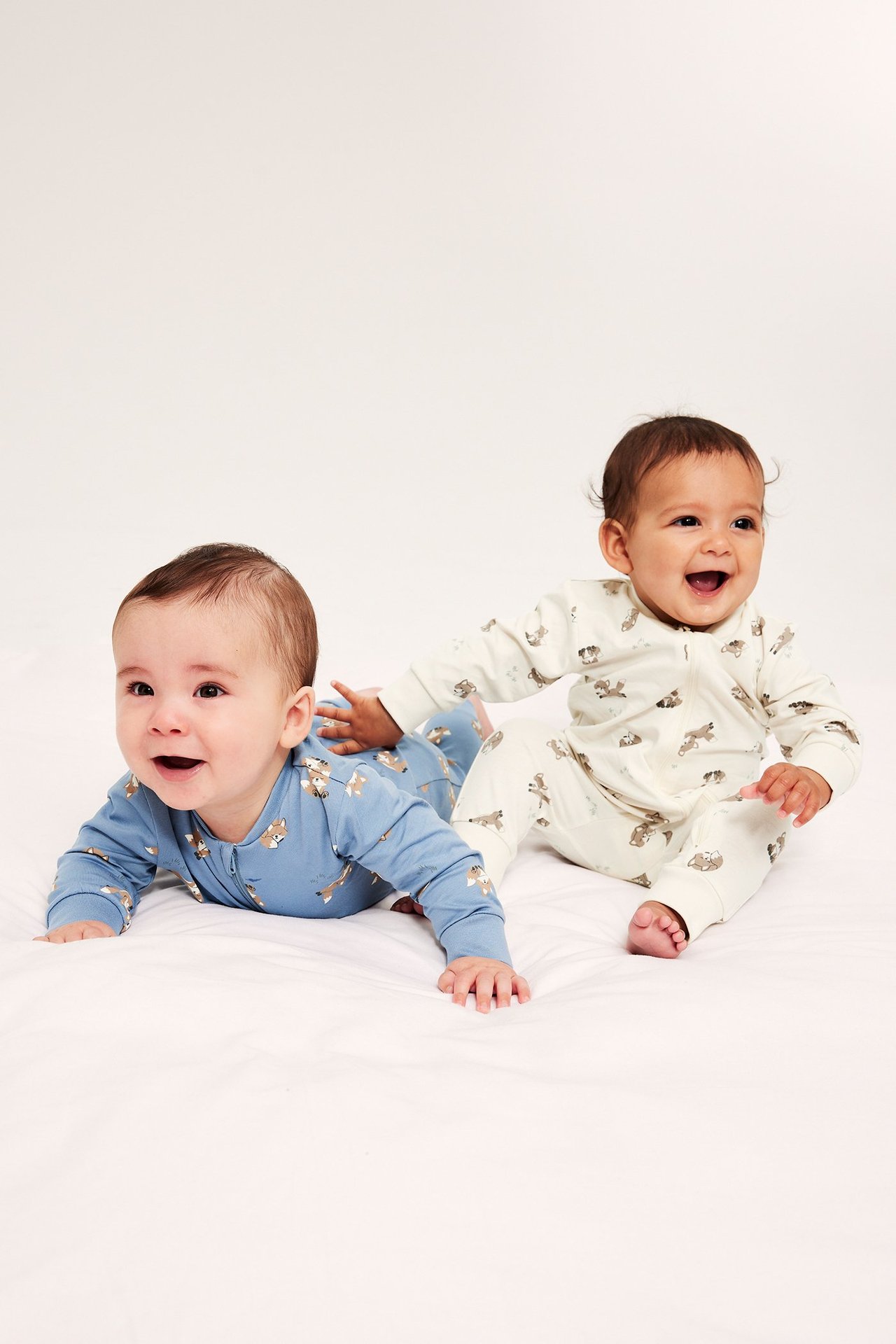 Edestäpäin: vauva sinisessä kuviollisessa potkupuvussa ja toinen kermanvärisessä.