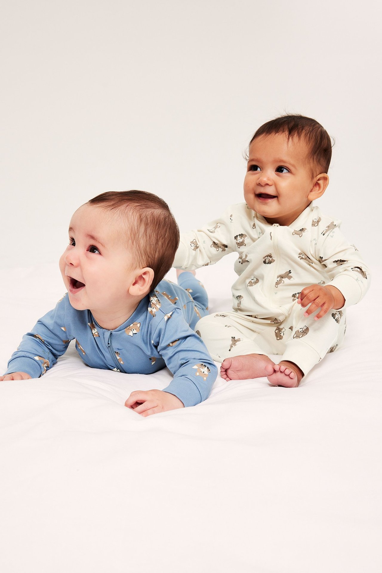 Widok z przodu dwóch niemowląt w wzorzystych pajacykach: niebieski i jasnobeżowy, oba z zamkiem.