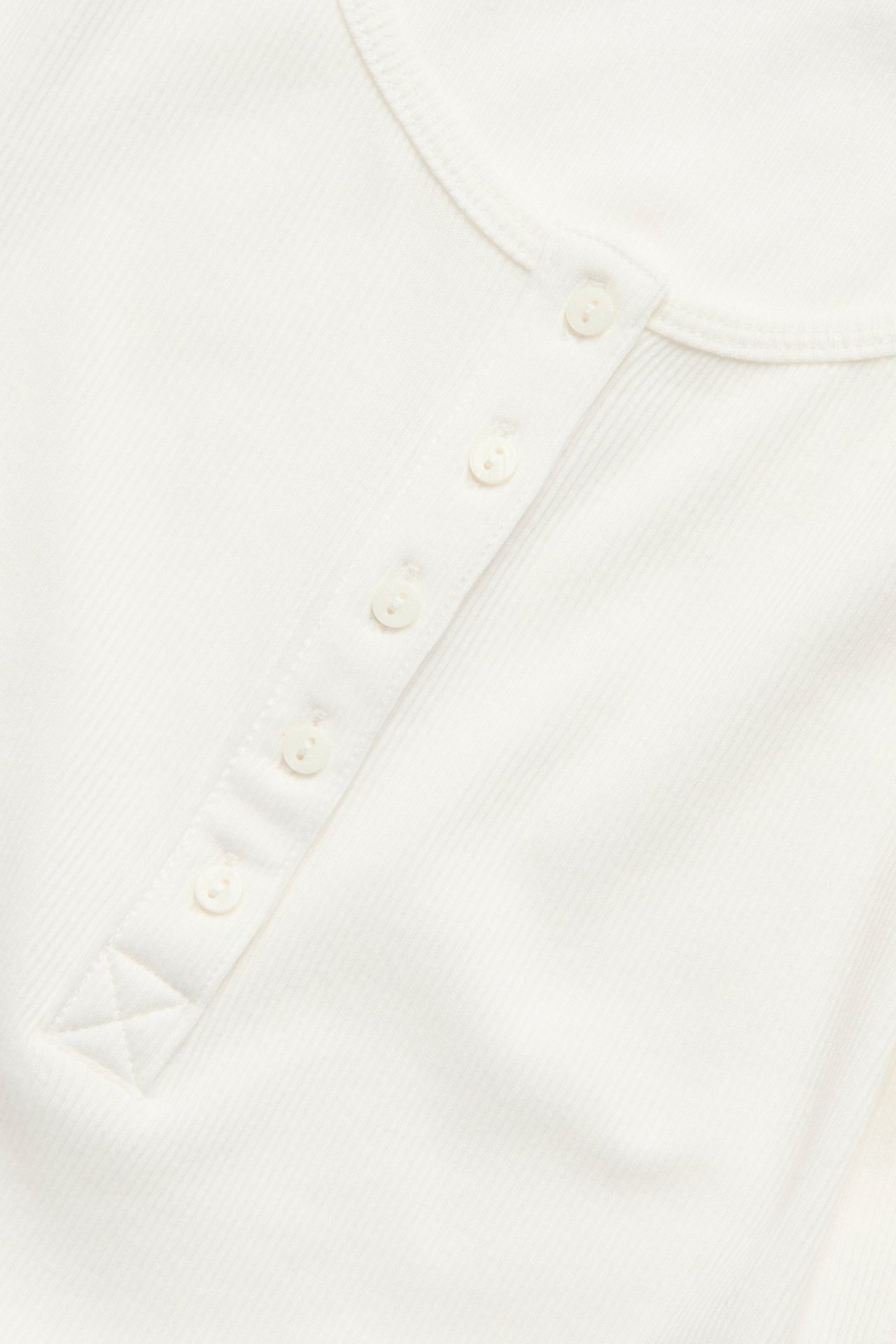 Zbliżenie na kremowy, prążkowany top z zapięciem na guziki z przodu.