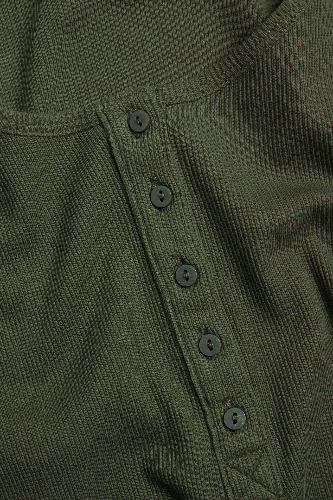 Zbliżenie zielonego prążkowanego topu z listwą guzikową z przodu i pasującymi guzikami.