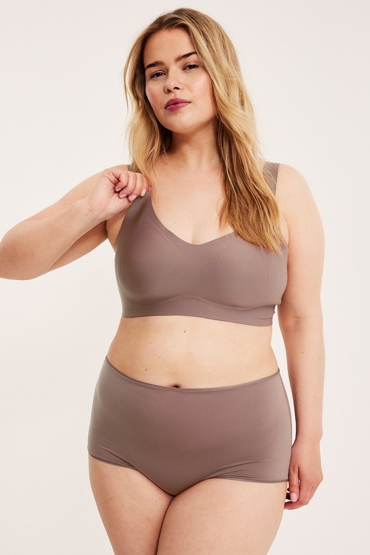 Frontvy av en kvinna i en mörkrosa bygellös mikro-bh med breda band och matchande trosa.