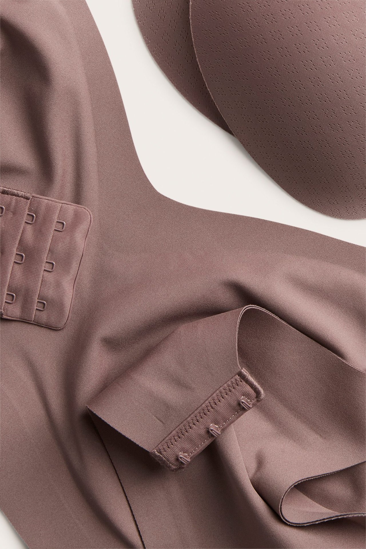 Zbliżenie na ciemnoróżowy, bezszwowy biustonosz bez fiszbin z zapięciem na haftki i wyjmowanymi wkładkami.