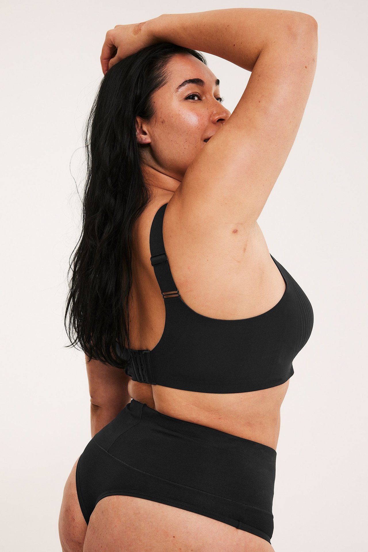 Sivukuva naisesta mustissa kaarituettomissa mikrokuituliiveissä ja vastaavissa mustissa pikkuhousuissa.