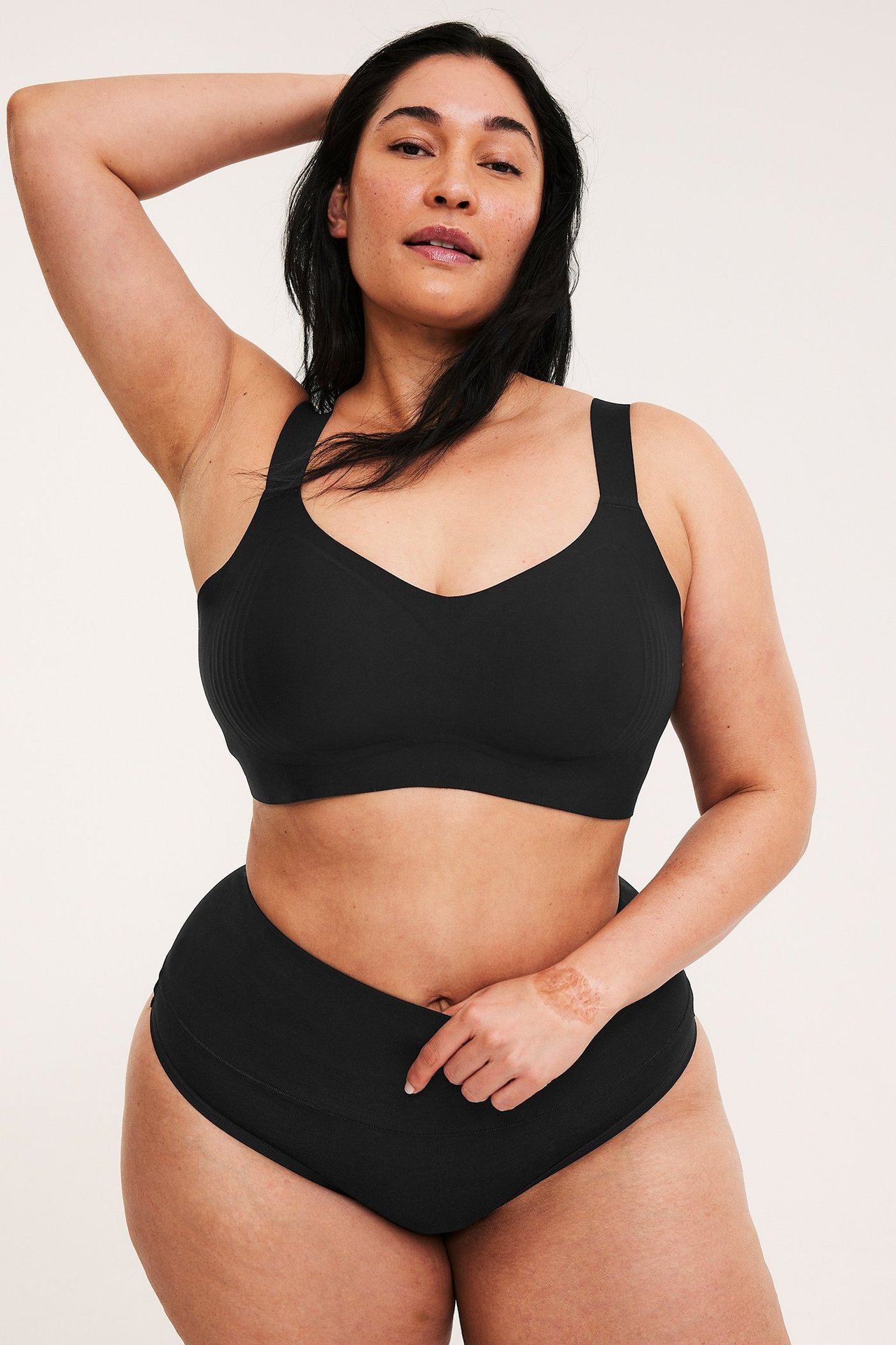 Nainen edestäpäin, mustassa kaarituettomassa mikro-rintaliiveissä ja yhteensopivissa korkeavyötäröisissä alushousuissa.