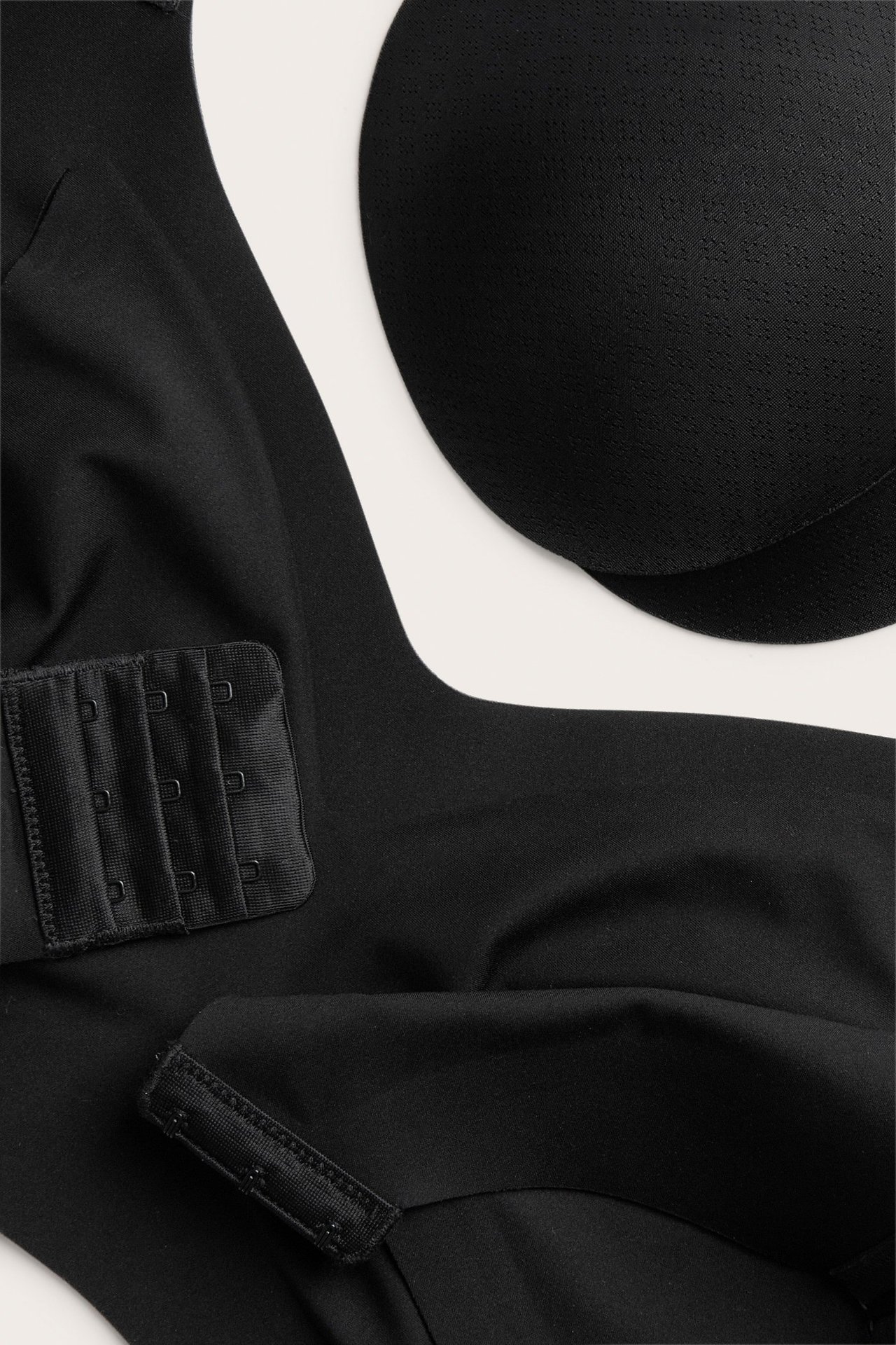 Zbliżenie czarnego biustonosza bez fiszbin z mikrofibry, z trójrzędowym zapięciem na haftki i wyjmowanymi wkładkami.