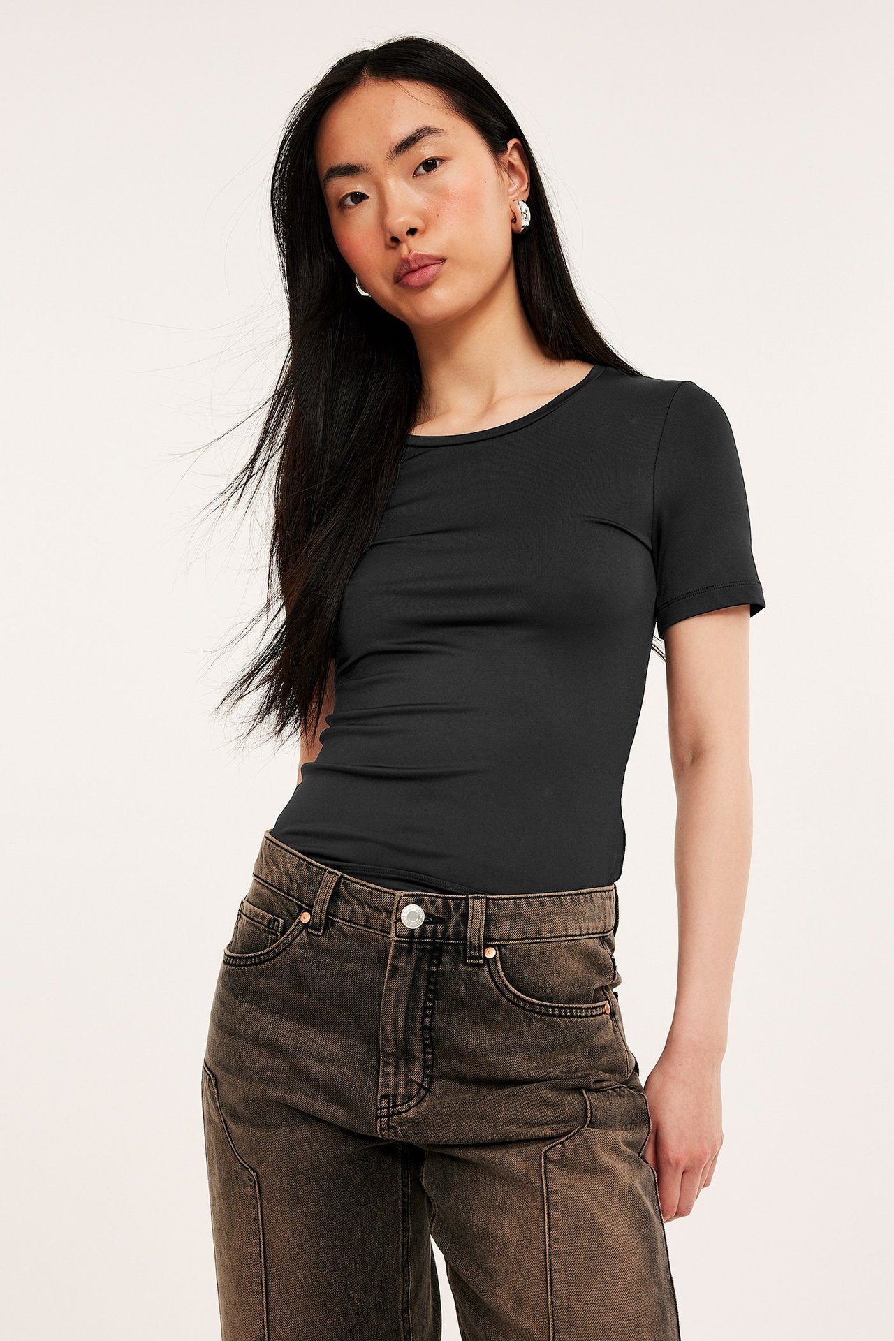 Frontbilde av kvinne i svart kortermet t-skjorte, mørkebrune jeans og sølvringer.