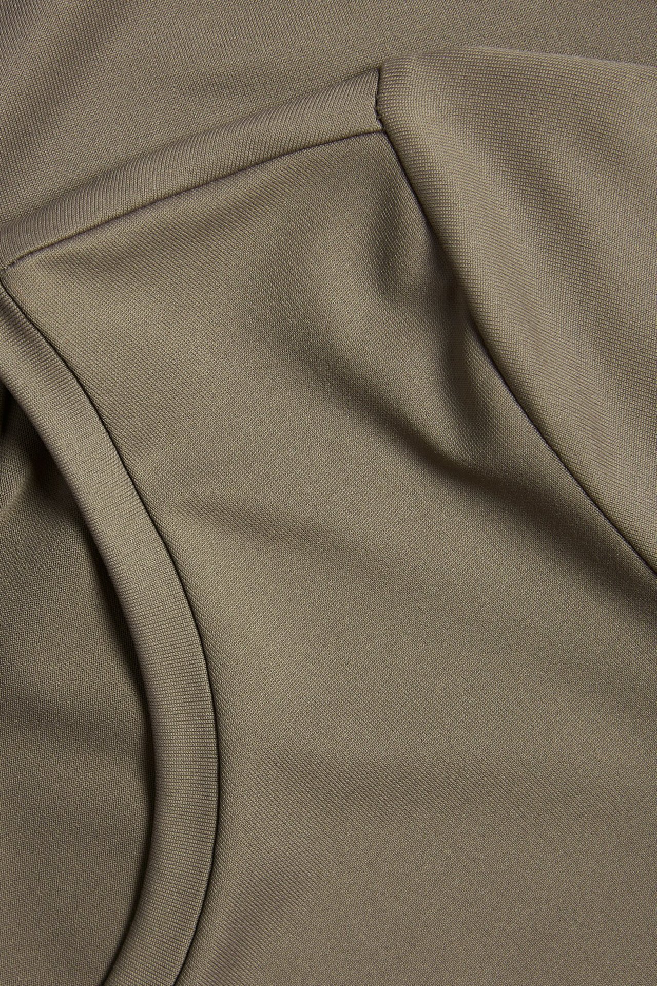 Zbliżenie brązowej tkaniny T-shirta z poliamidu i elastanu, ukazujące szew okrągłego dekoltu i teksturę.