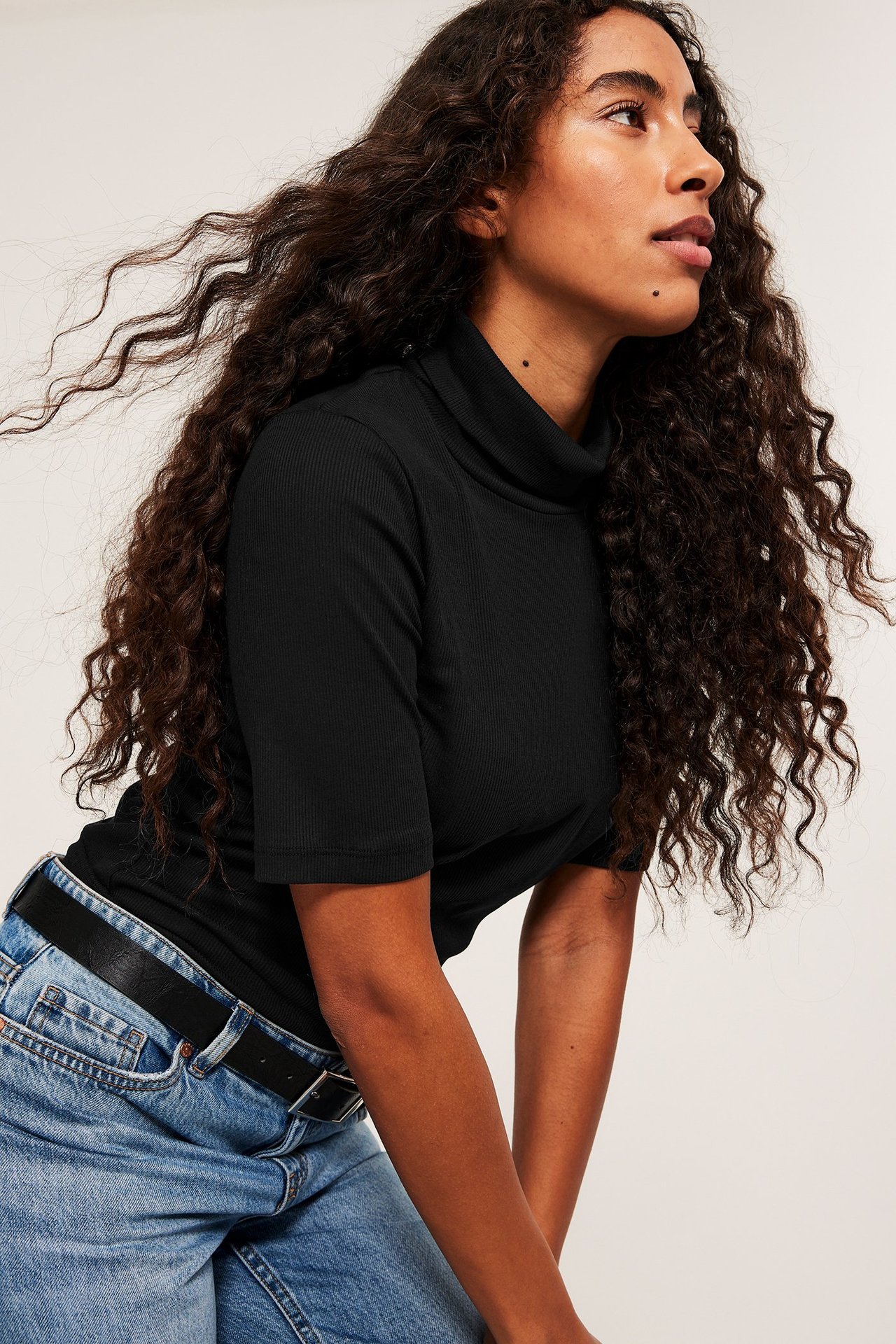 Kobieta w czarnej prążkowanej turtleneck z fakturą, widok z przodu, w jeansach.