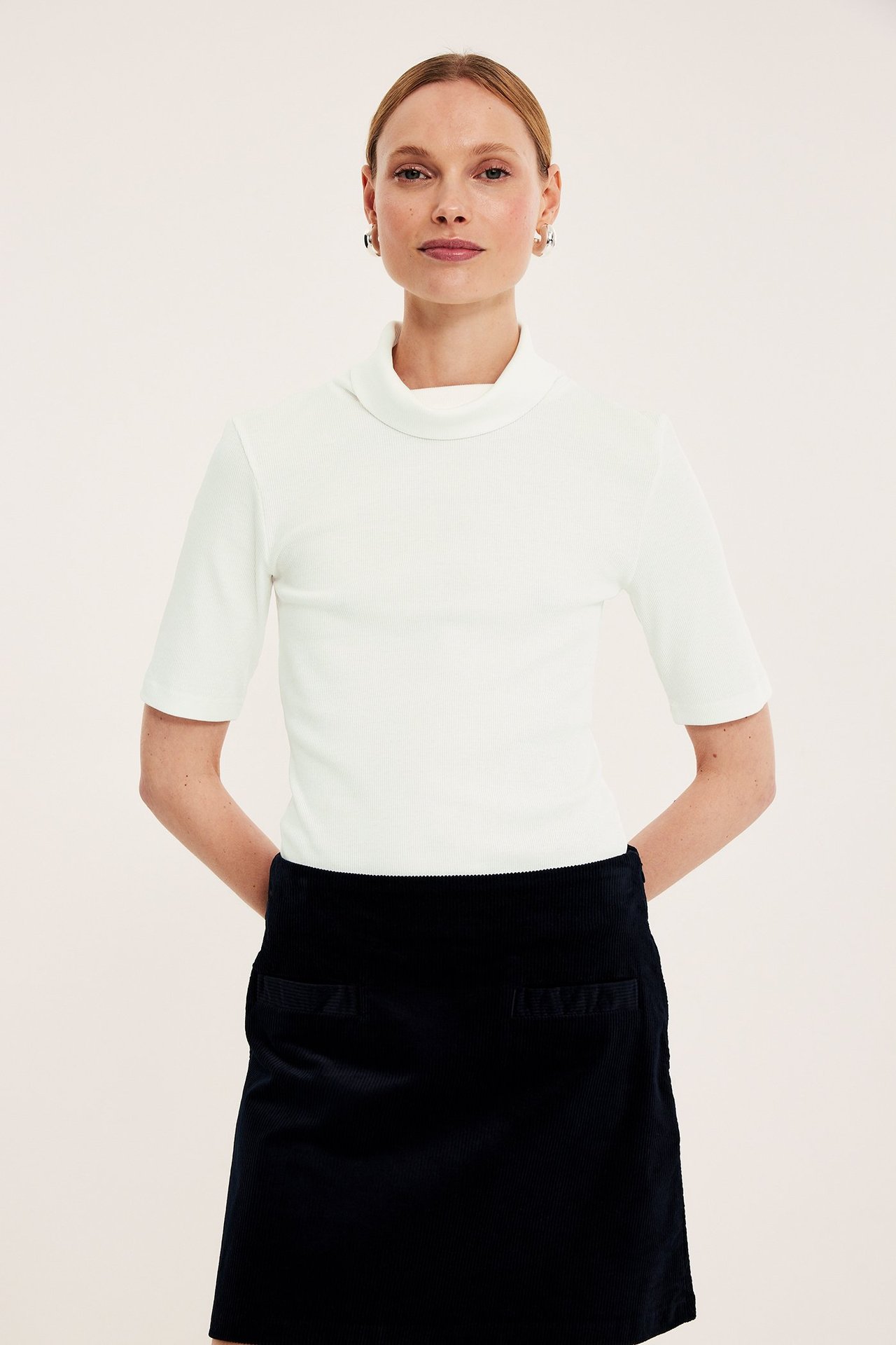 Edestä, nainen yllään luonnonvalkoinen ribbineulepoolopaita, tummansininen vakosamettihame ja hopeiset korvarenkaat.