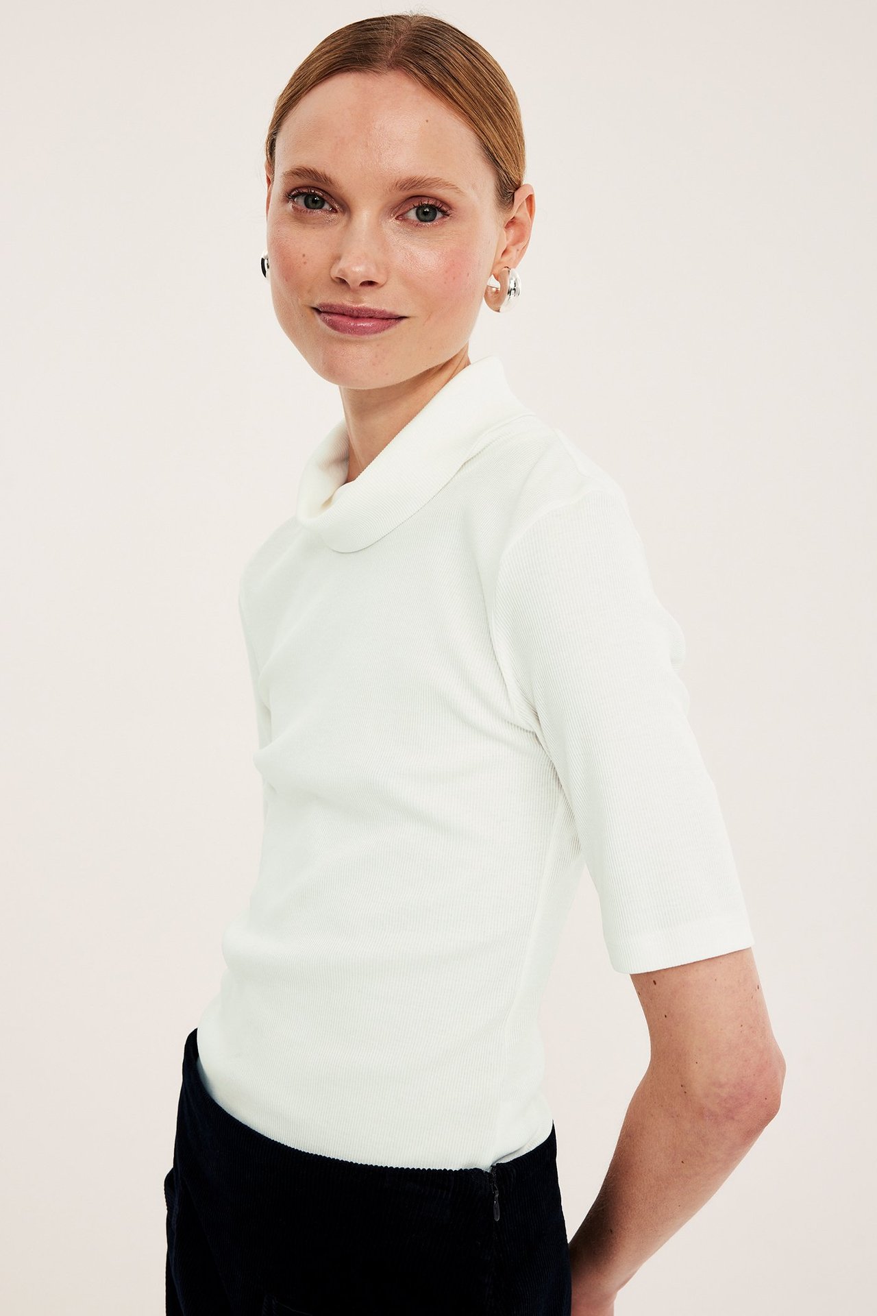 Naisen etuviisto kuva: luonnonvalkoinen ribattu poolopaita kyynärpääpituisilla hihoilla ja hopeakorvakorut.