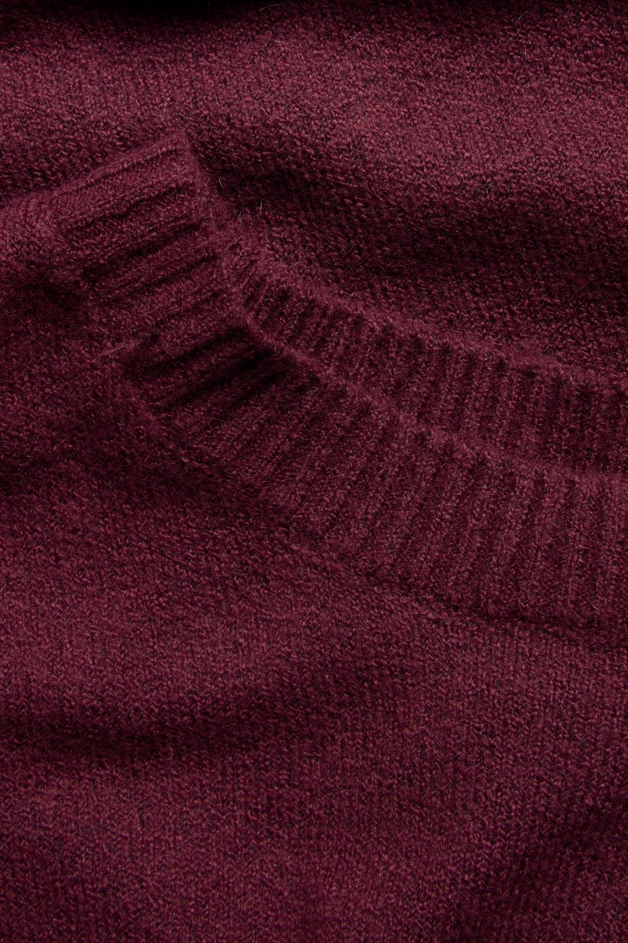 Zbliżenie na melanżową, bordową sukienkę dzianinową, ukazujące prążkowany dekolt.