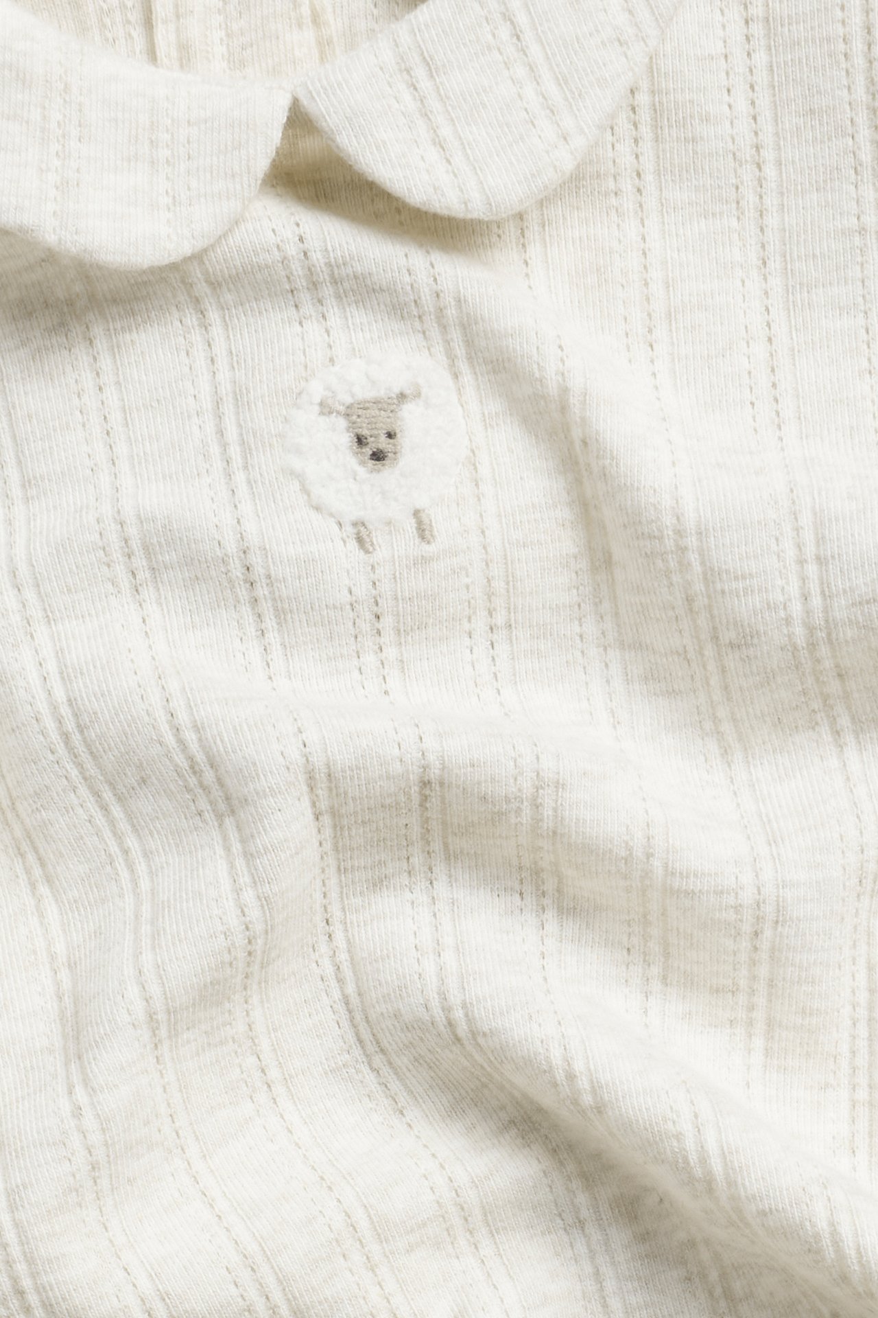 Närbild på en beige melerad ribbad babybody med rund krage och broderat får.