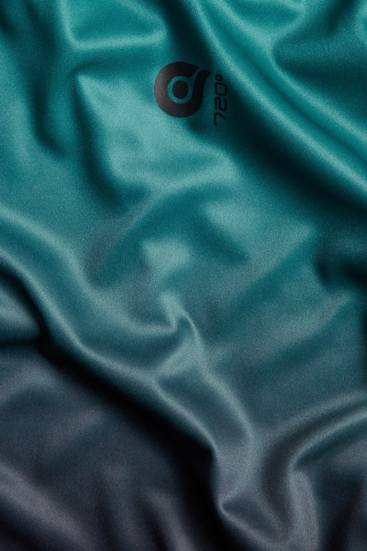 Zbliżenie zielonej, ombre poliestrowej koszulki sportowej z małym czarnym nadrukiem graficznym na piersi.