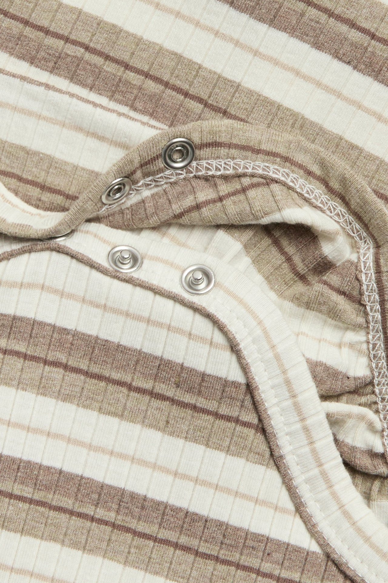 Lähikuva beigestä ja valkoisesta raidallisesta ribbineuleisesta vauvanbodysta, jossa hopeiset nepparit.